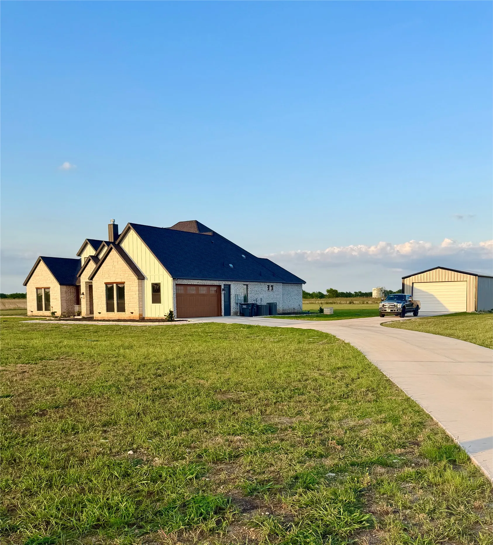 Exterior featuring a dark shingle roof, light-toned brick and vertical siding, a wood-finish garage door, and an extended concrete driveway