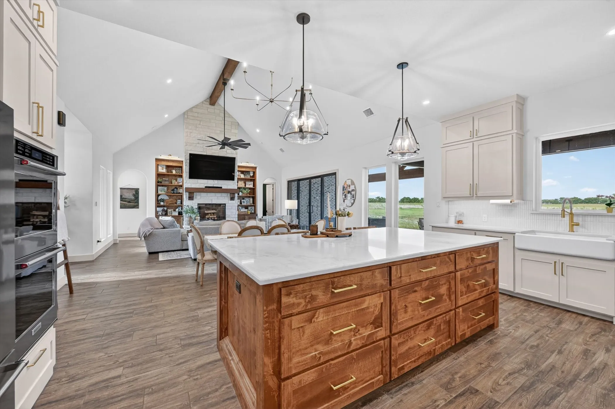 Open-concept kitchen featuring a large wood-finish island with a white countertop, two pendant light fixtures, and a farmhouse sink