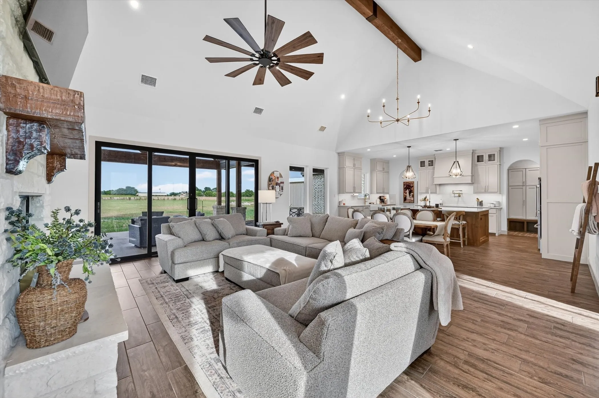Spacious living area featuring high vaulted ceilings with exposed wood beams, a large sliding glass door system, and wood look tile flooring