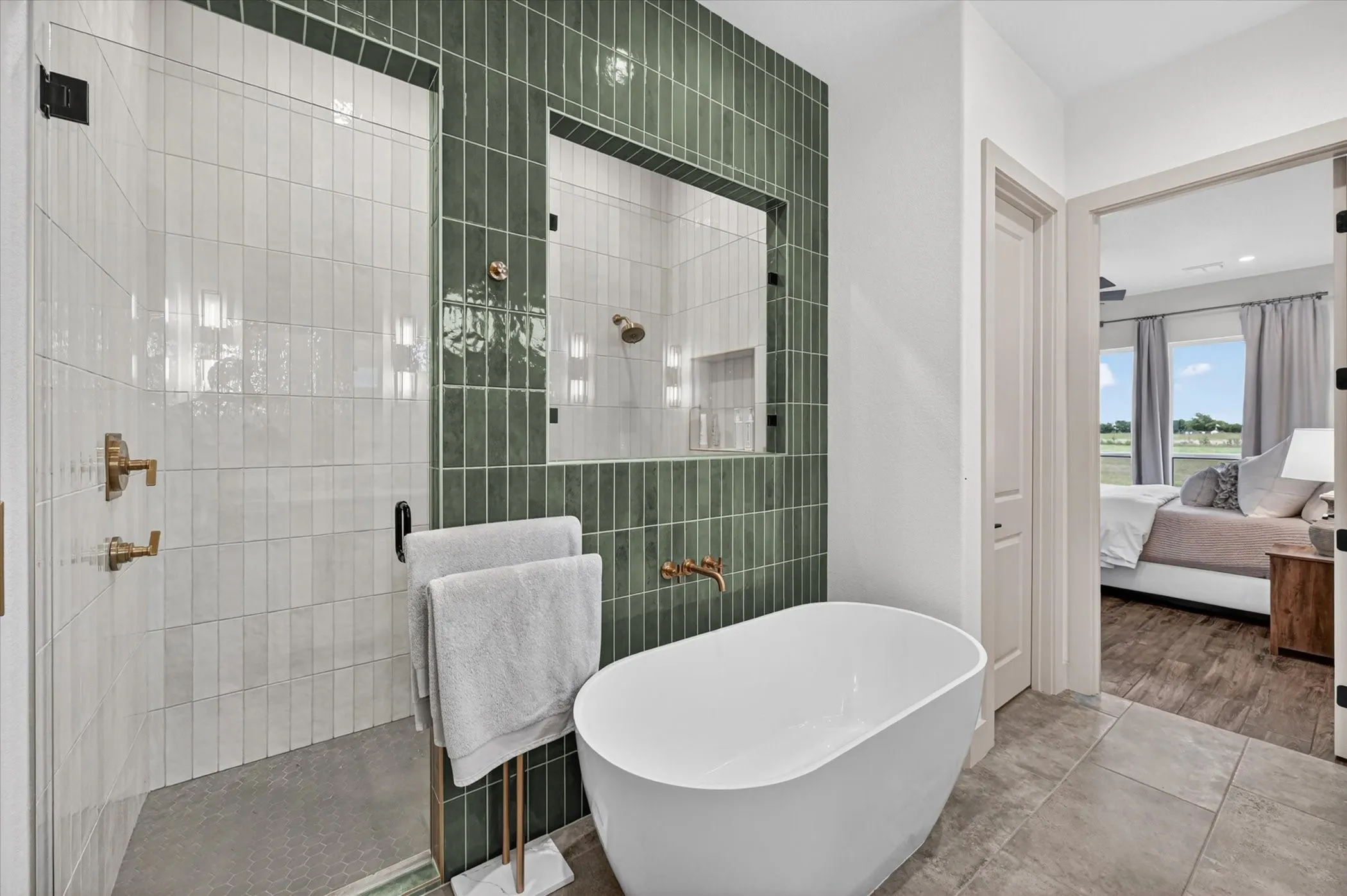 Freestanding soaking tub with a wall-mounted brass faucet, complemented by a walk-in shower featuring a glass enclosure and a textured green tile accent wall