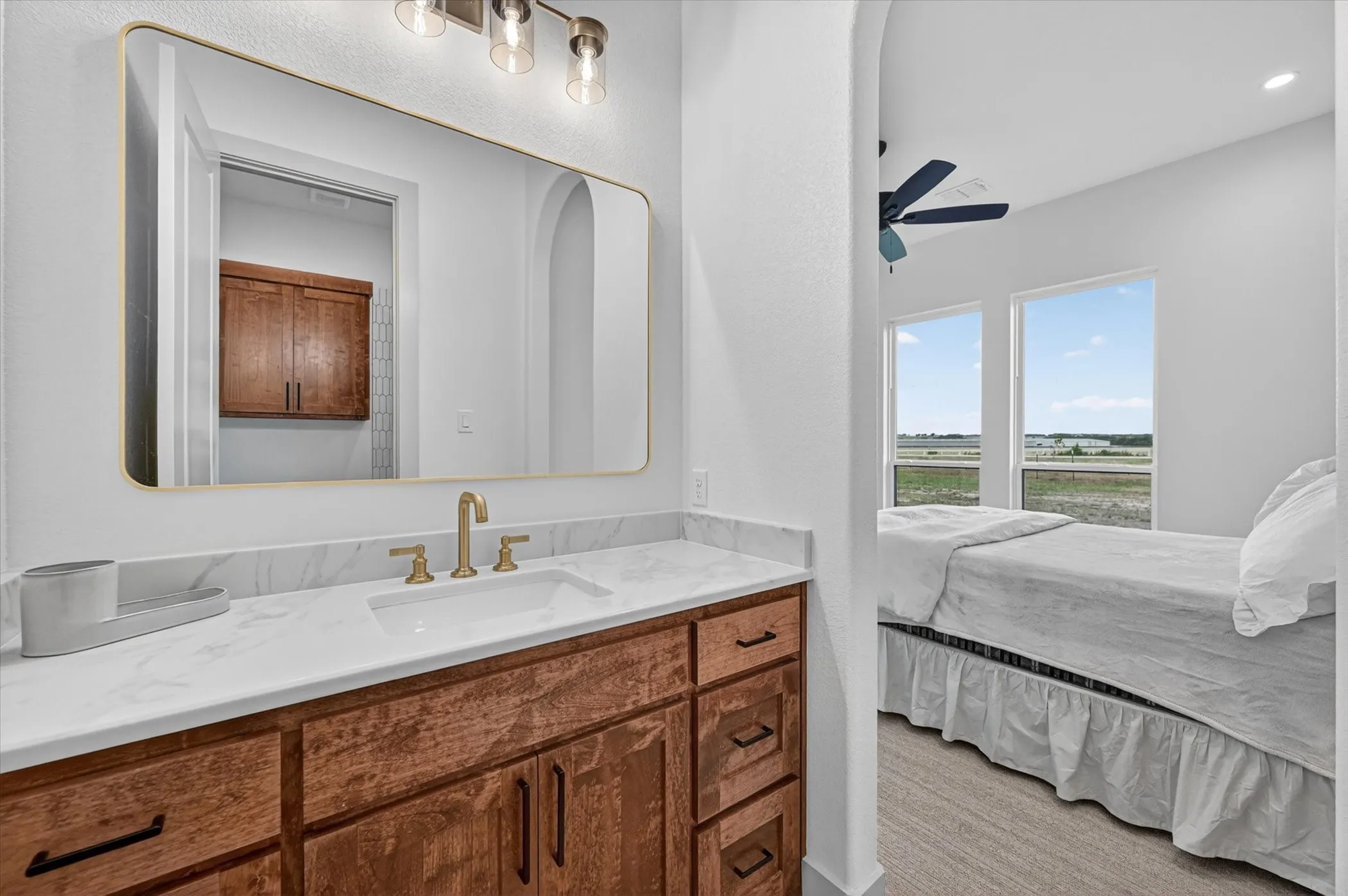 White vanity with a rectangular undermount sink, brushed gold-finish faucet, and a large framed mirror