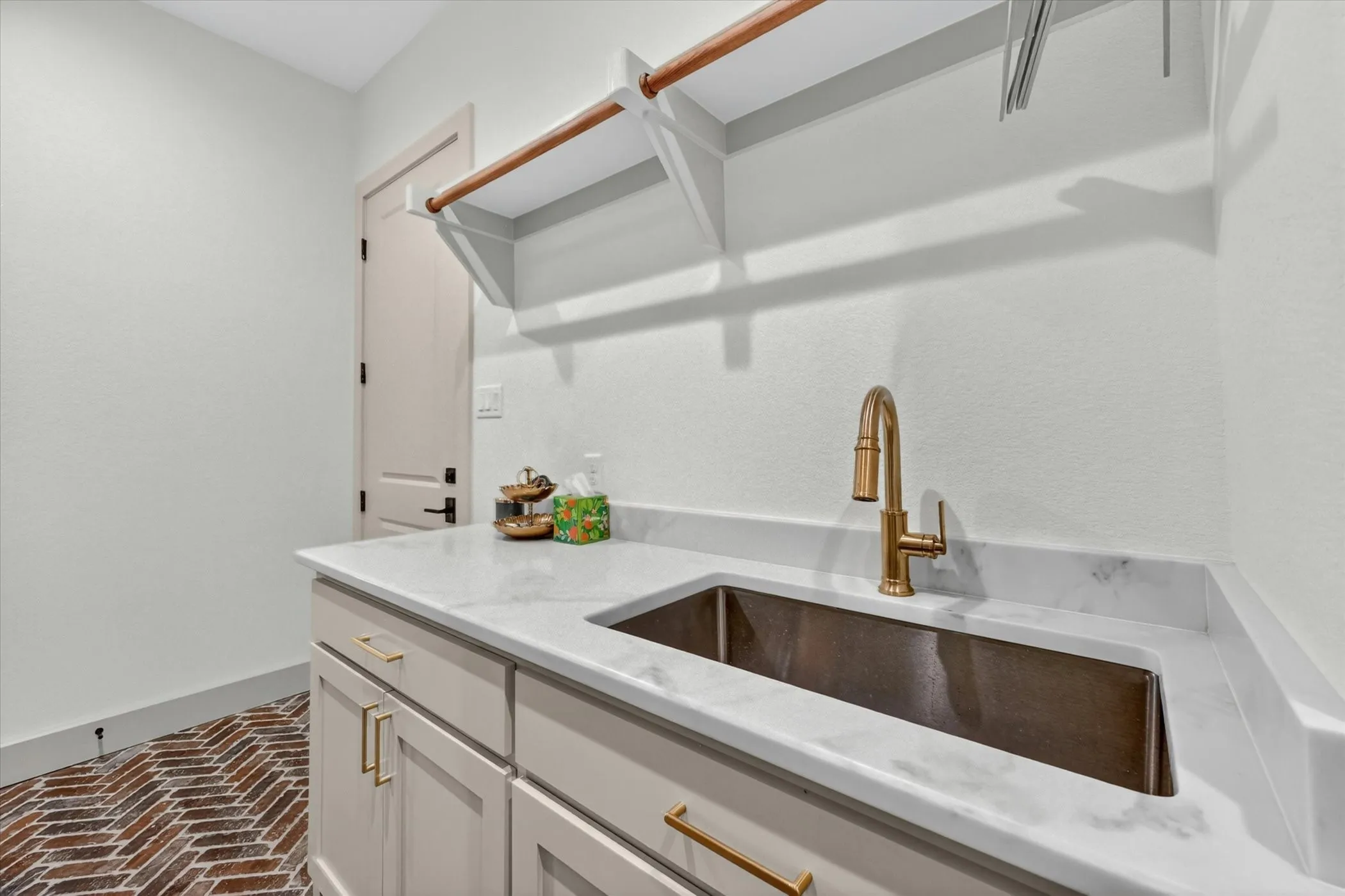 Herringbone brick-patterned flooring complements a light-beige cabinetry gold-finish hardware