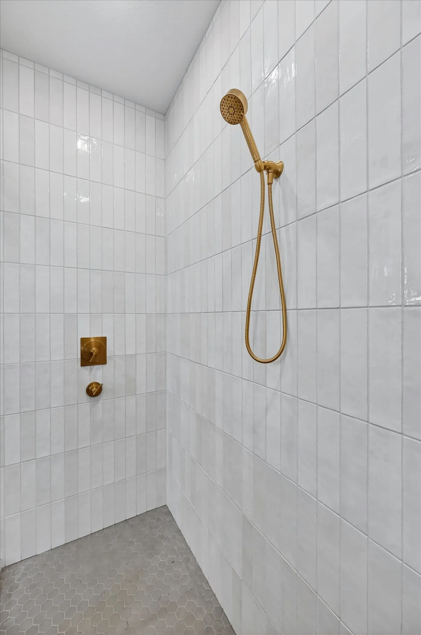Walk-in shower featuring white subway tile walls, a hand-held shower fixture, and a wall-mounted shower control with a brushed gold finish
