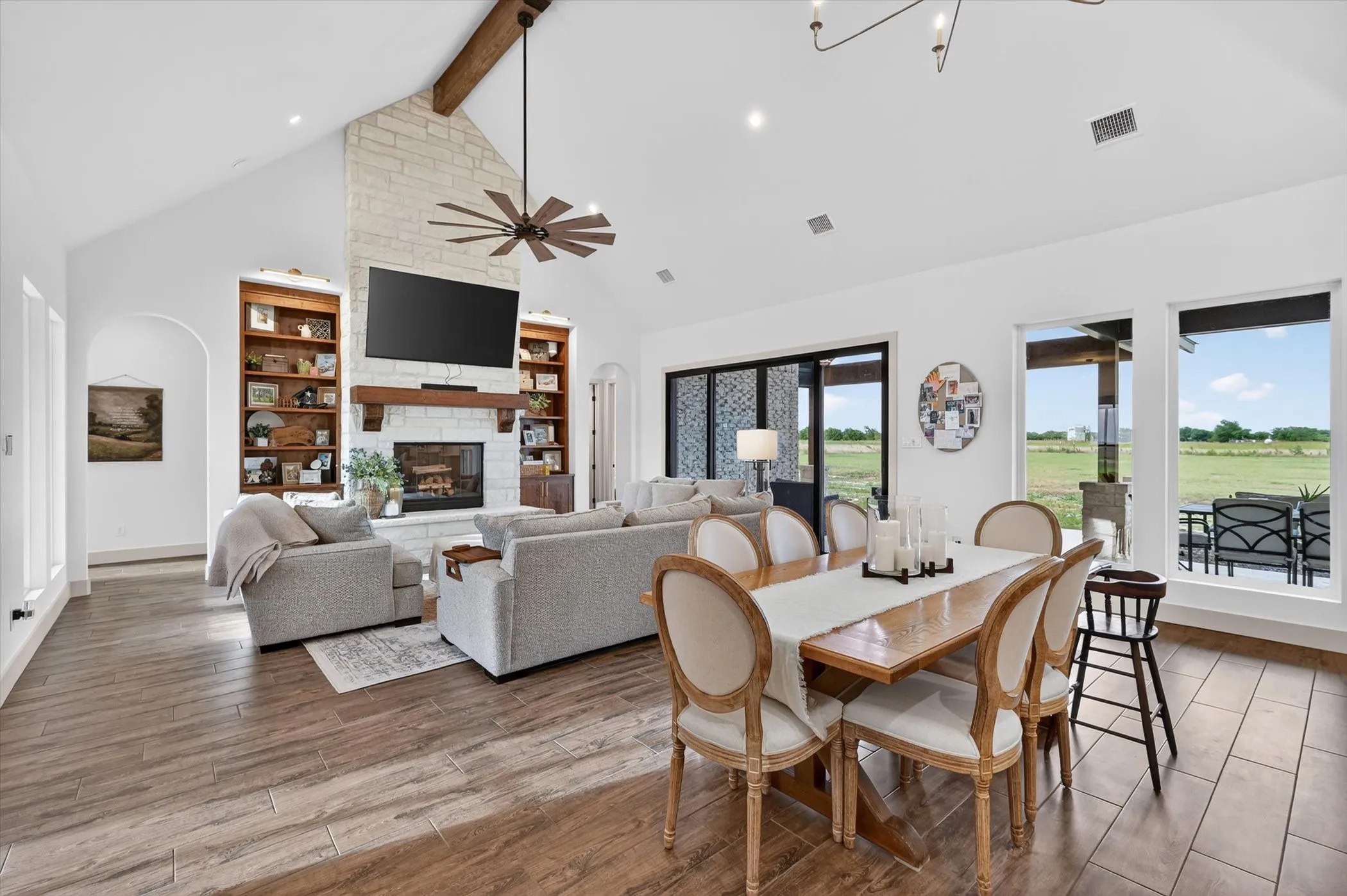 Spacious open-concept living area featuring a stone-clad fireplace with a wood mantle, vaulted ceilings with an exposed wood beam, recessed lighting, and wood-look tile flooring
