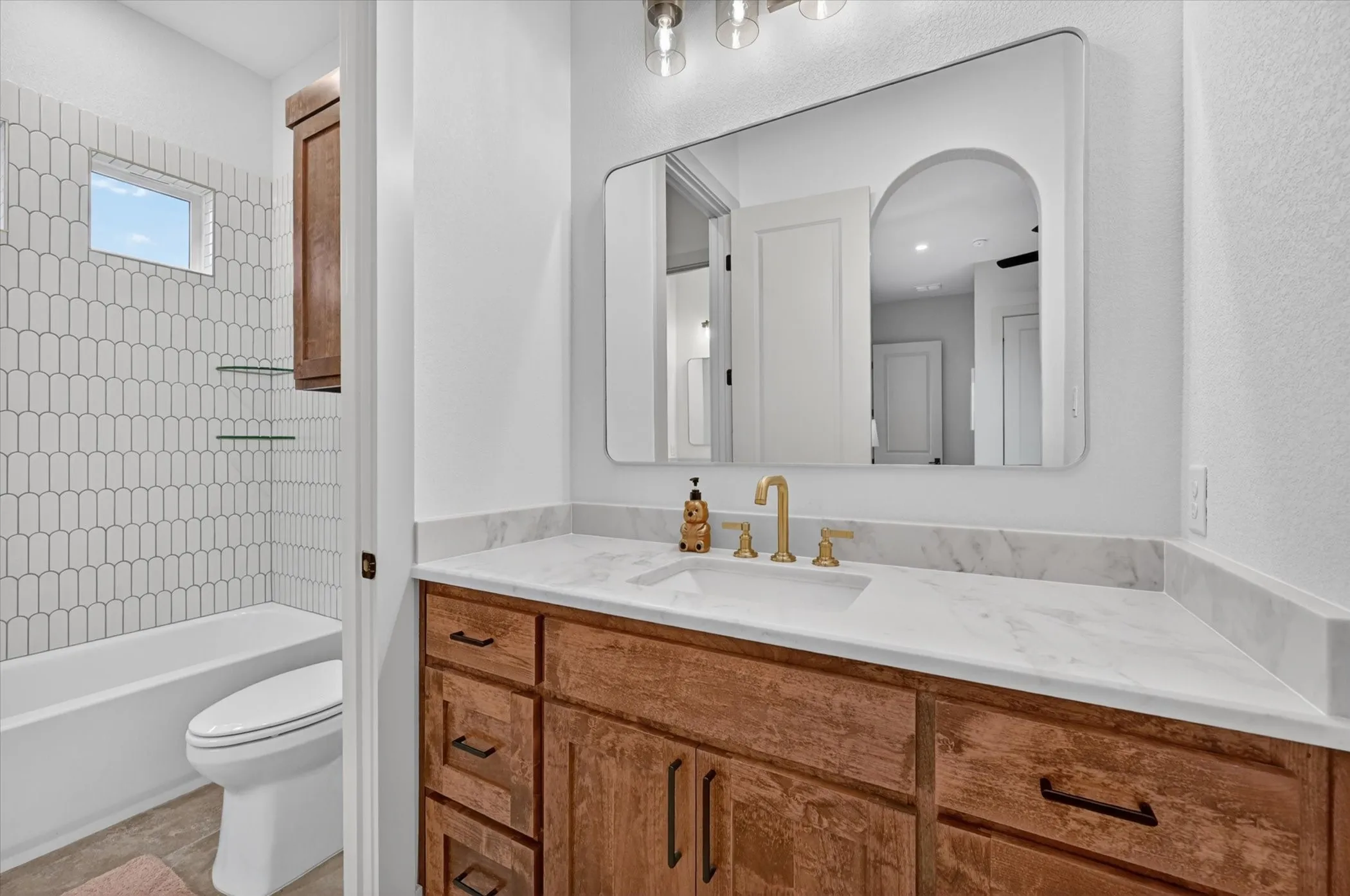 Bathroom featuring a wood-finish vanity with a single basin, a light-toned countertop, and a contemporary wall-mounted mirror