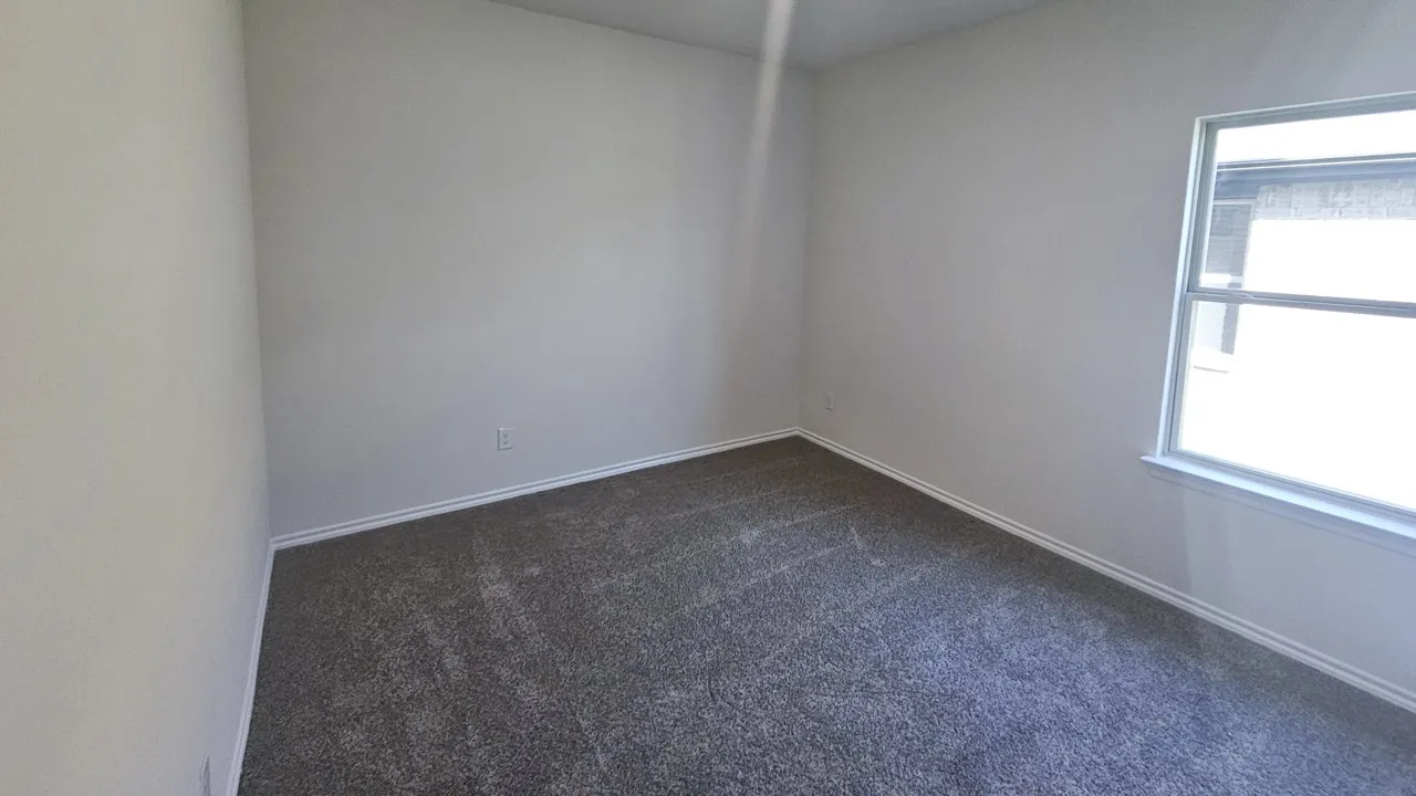 Bright room featuring neutral wall paint, gray patterned carpet, a single window, and white baseboards