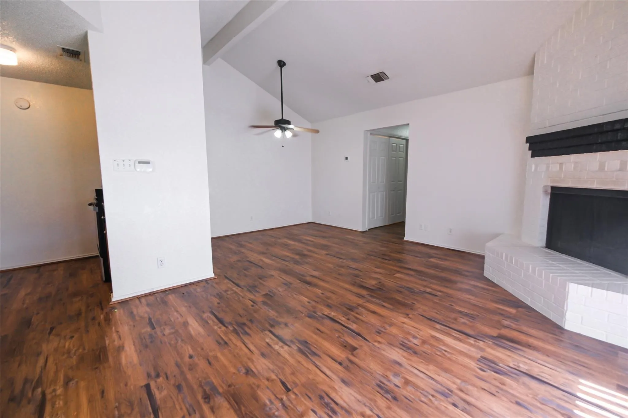 Spacious living area featuring wood-finish flooring, a vaulted ceiling, and a ceiling fan with integrated lighting