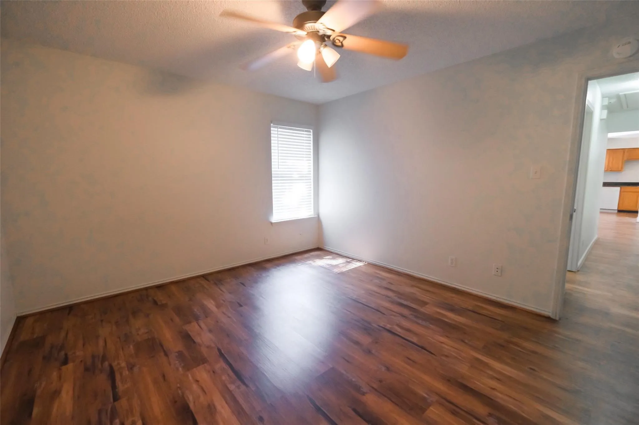 Room featuring wood-finish flooring, a ceiling fan with integrated lighting, and a single window with horizontal blinds