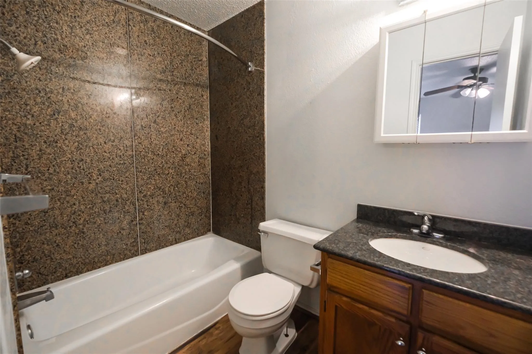 Bathroom featuring a tub/shower combination with a textured surround, a white toilet, and wood-finish flooring