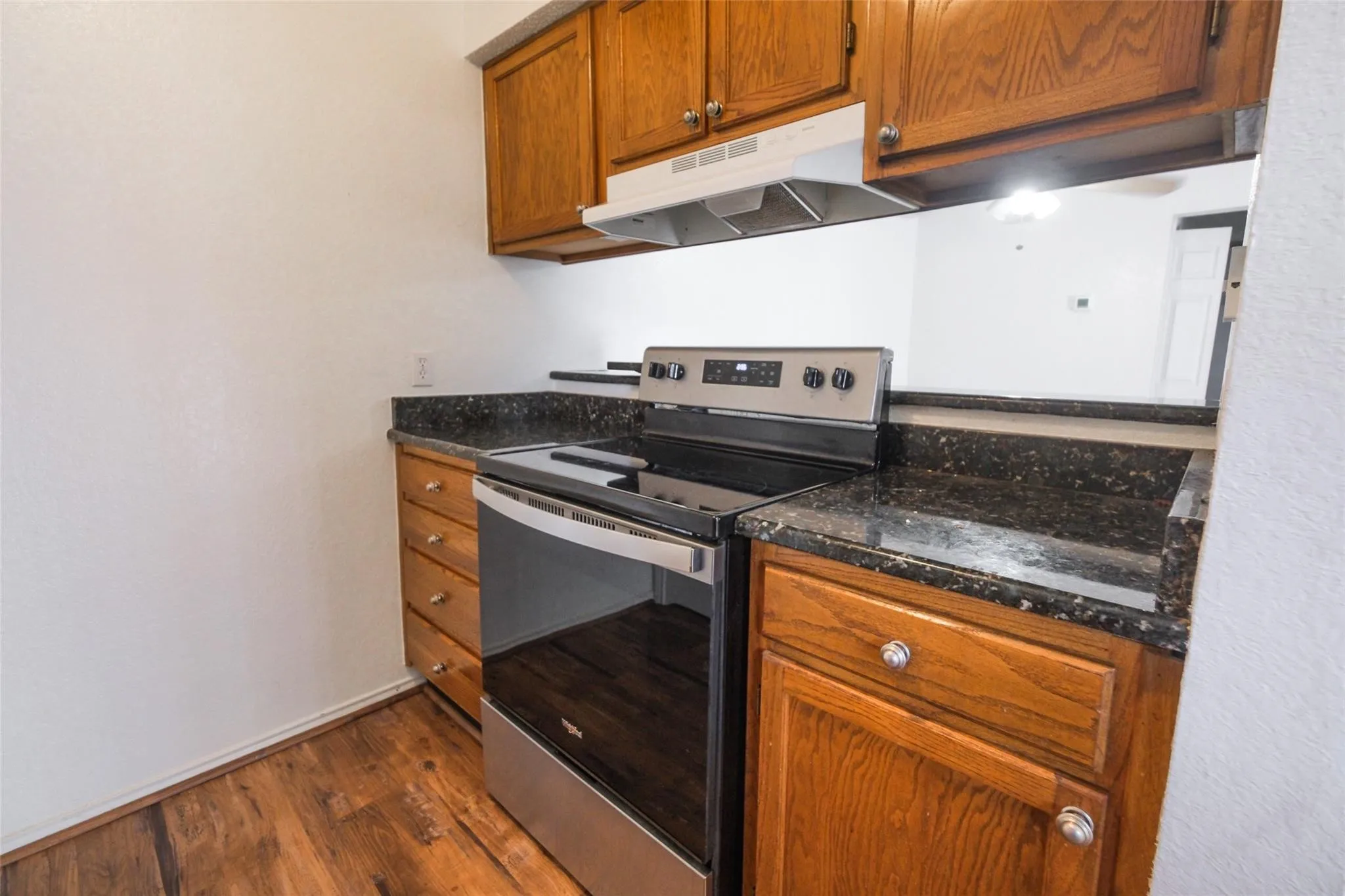 Kitchen featuring wood-finish flooring, dark speckled countertops, and wood cabinetry with silver hardware