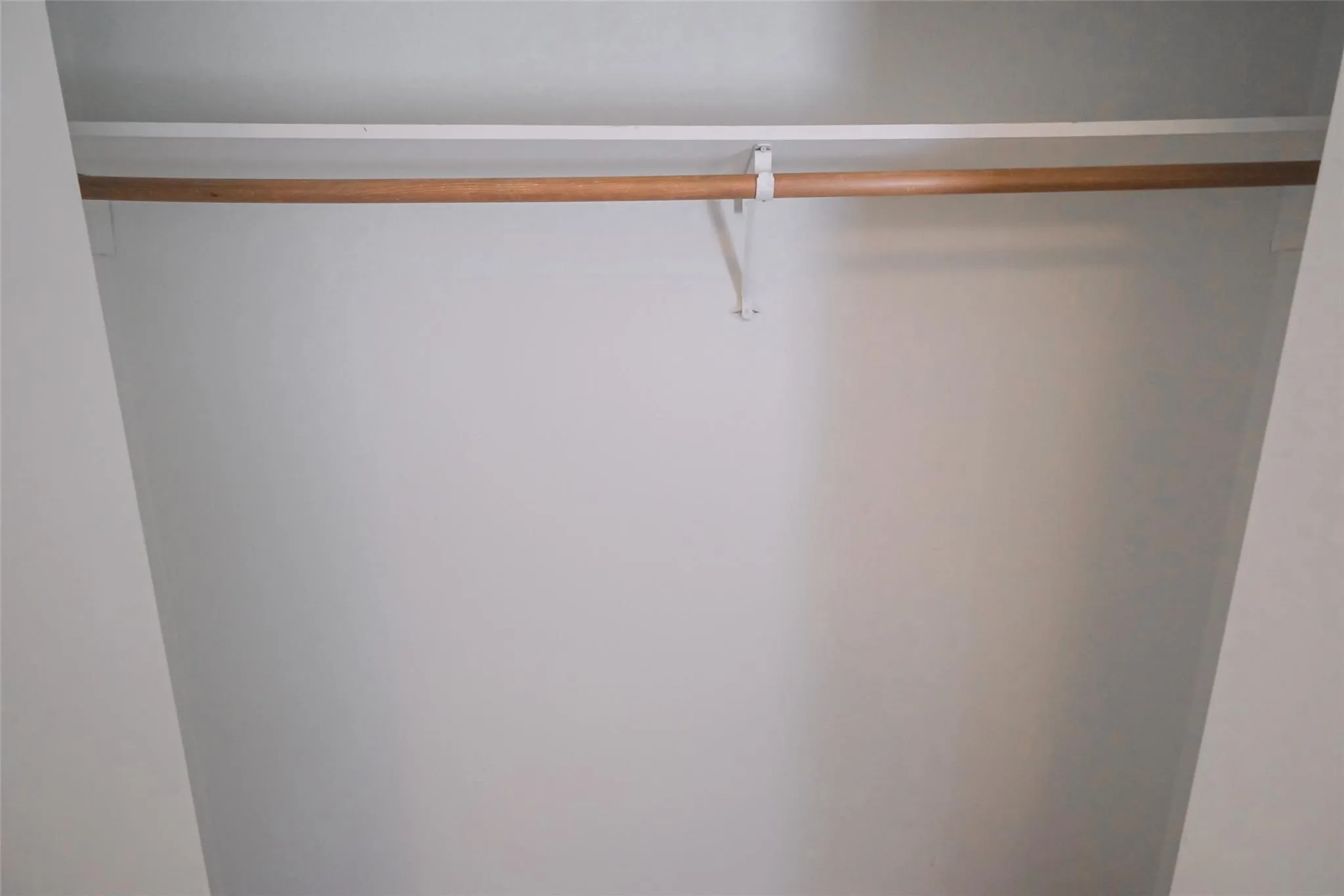 Closet featuring a wooden hanging rod and upper storage shelf