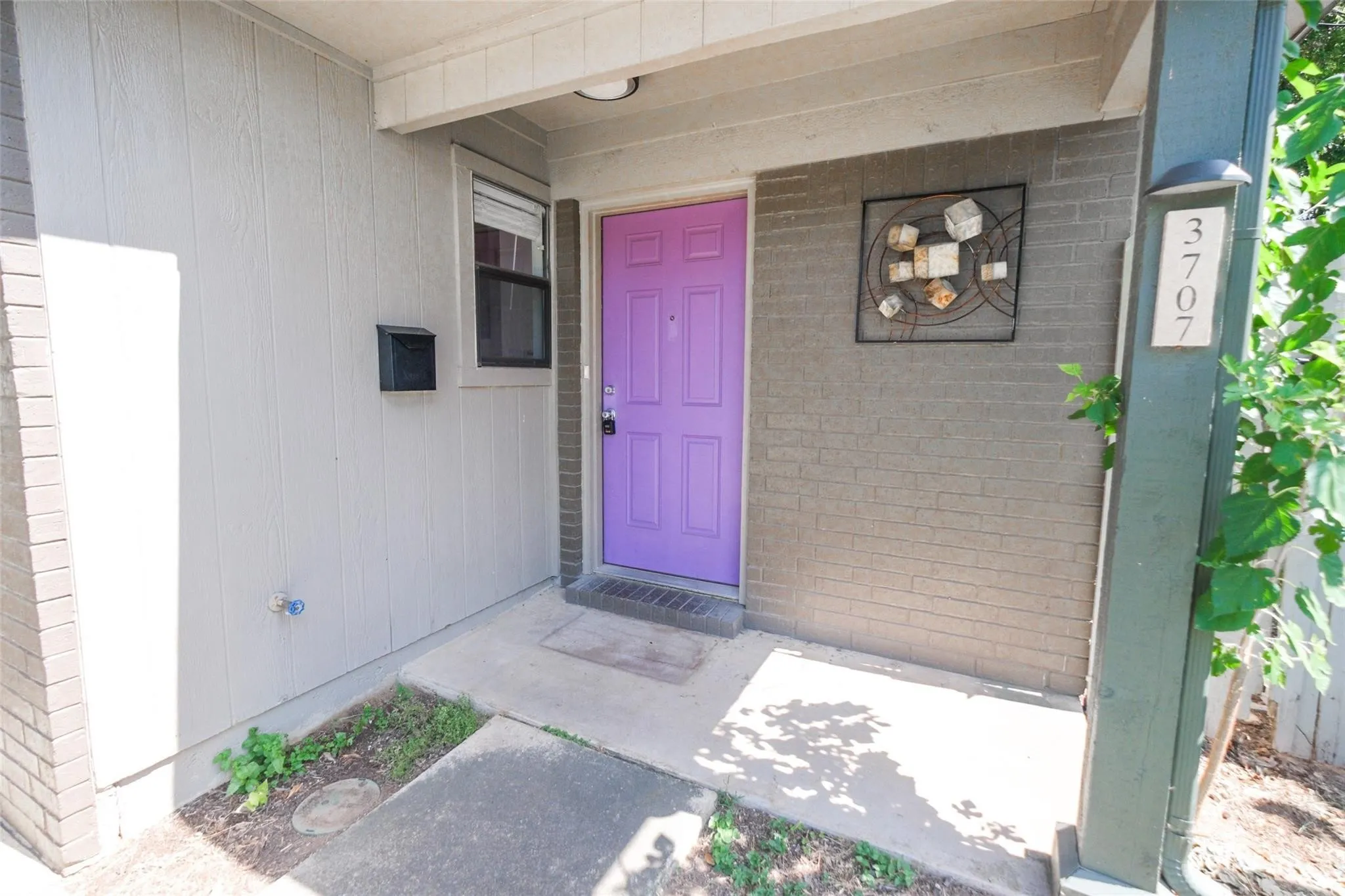 Inviting front entry featuring a vibrant purple door, mixed material facade, recessed overhead lighting, and prominent house numbers
