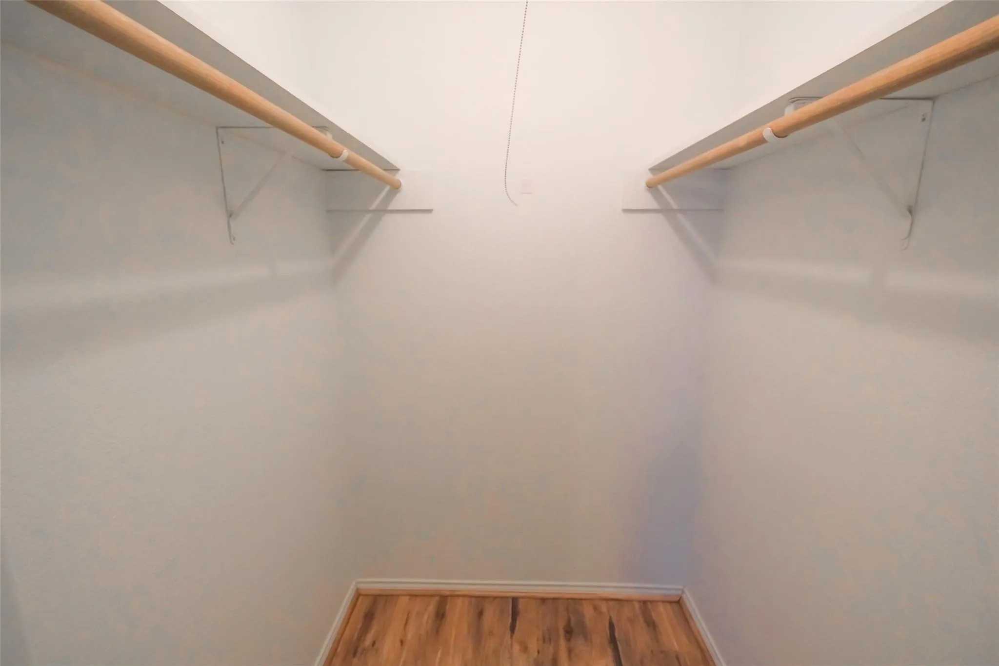 Walk-in closet featuring light wood-finish flooring, white walls, and dual wooden hanging rods with white support brackets