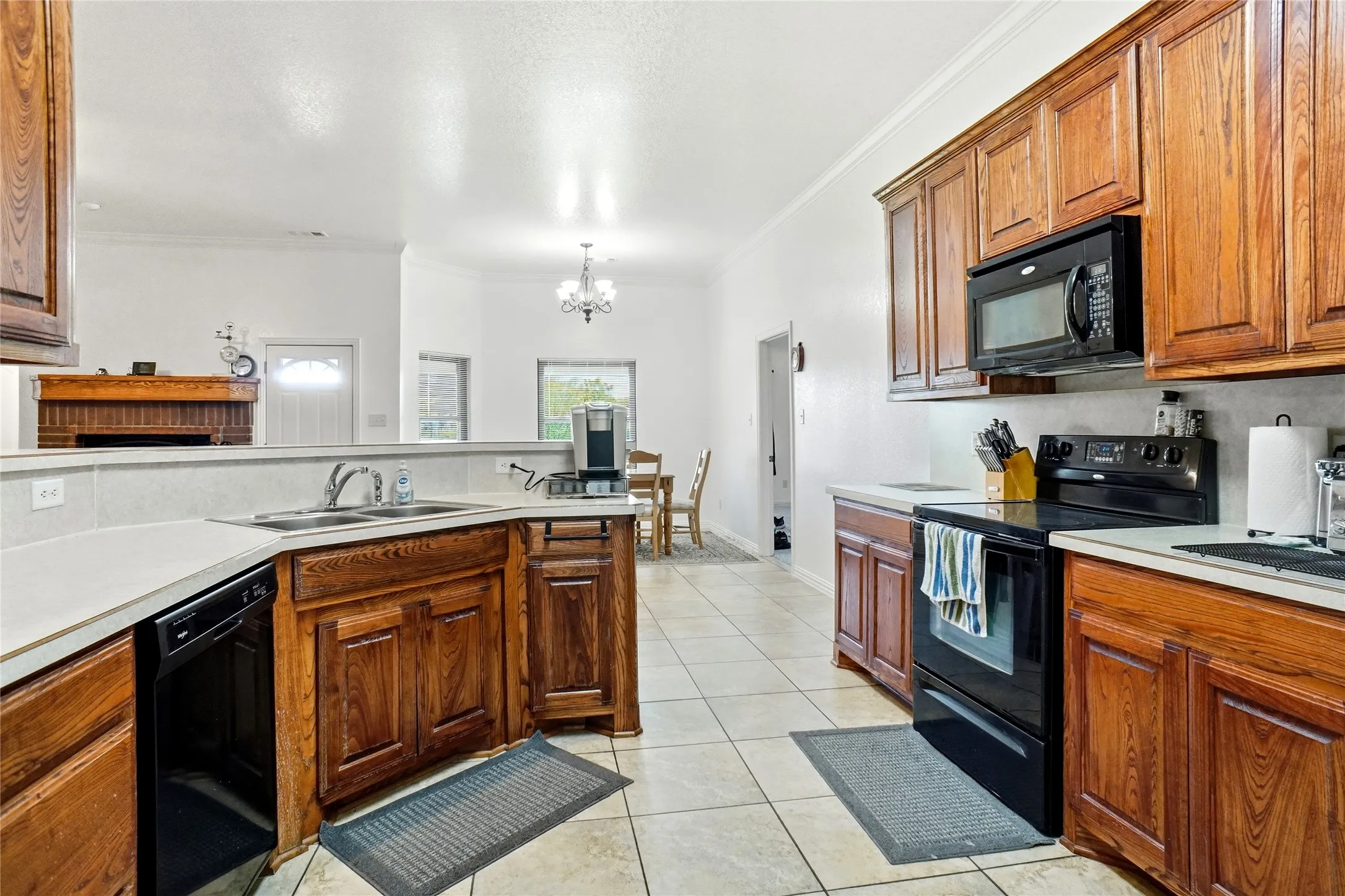 Kitchen featuring wood cabinetry, white countertops, stainless steel sink, black built-in microwave, and tile flooring