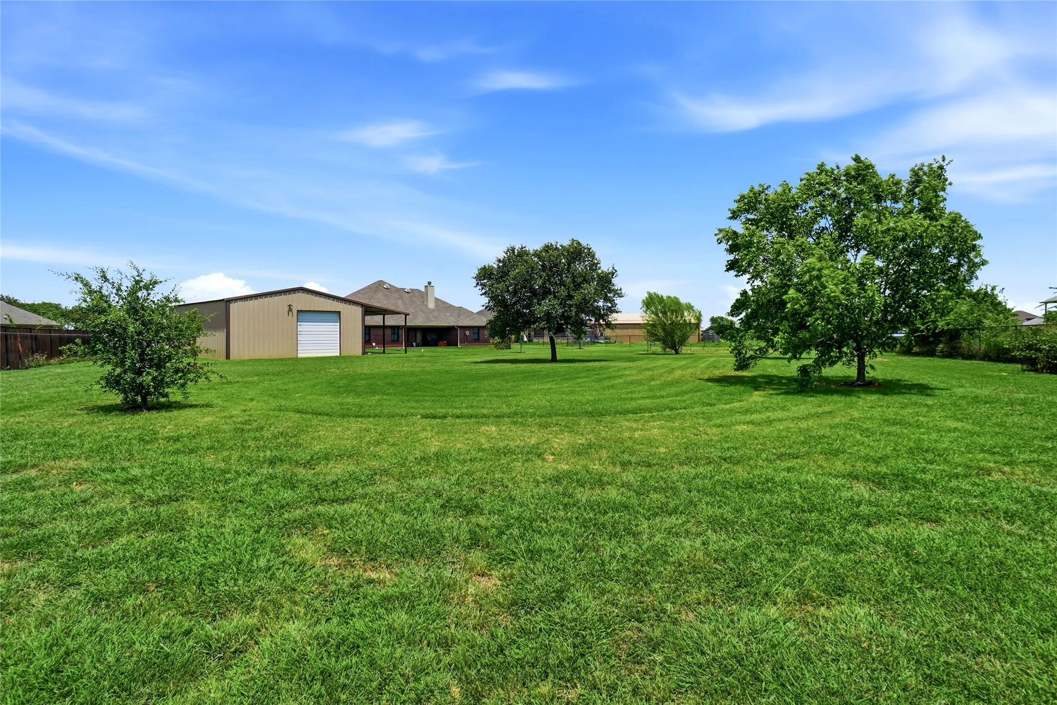Spacious backyard featuring a manicured lawn, several mature trees, and a detached metal building with a roll-up door