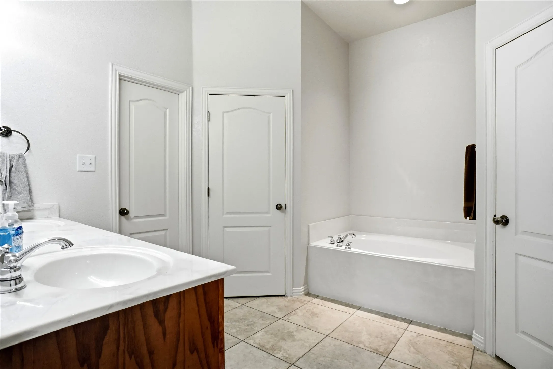 Bathroom featuring a built-in soaking tub, a vanity with a white countertop and integrated sink, wood-finish cabinetry, and square tiled flooring