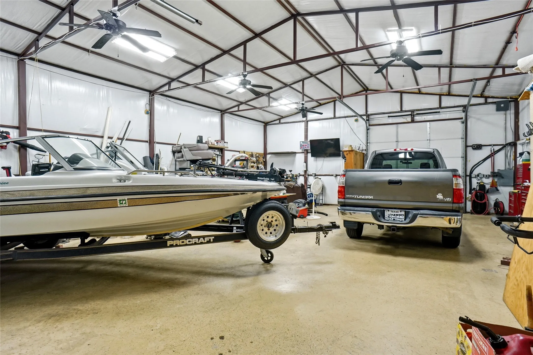 Spacious workshop with high ceilings, multiple ceiling fans, exposed metal beam construction, bright overhead lighting, and two large garage doors