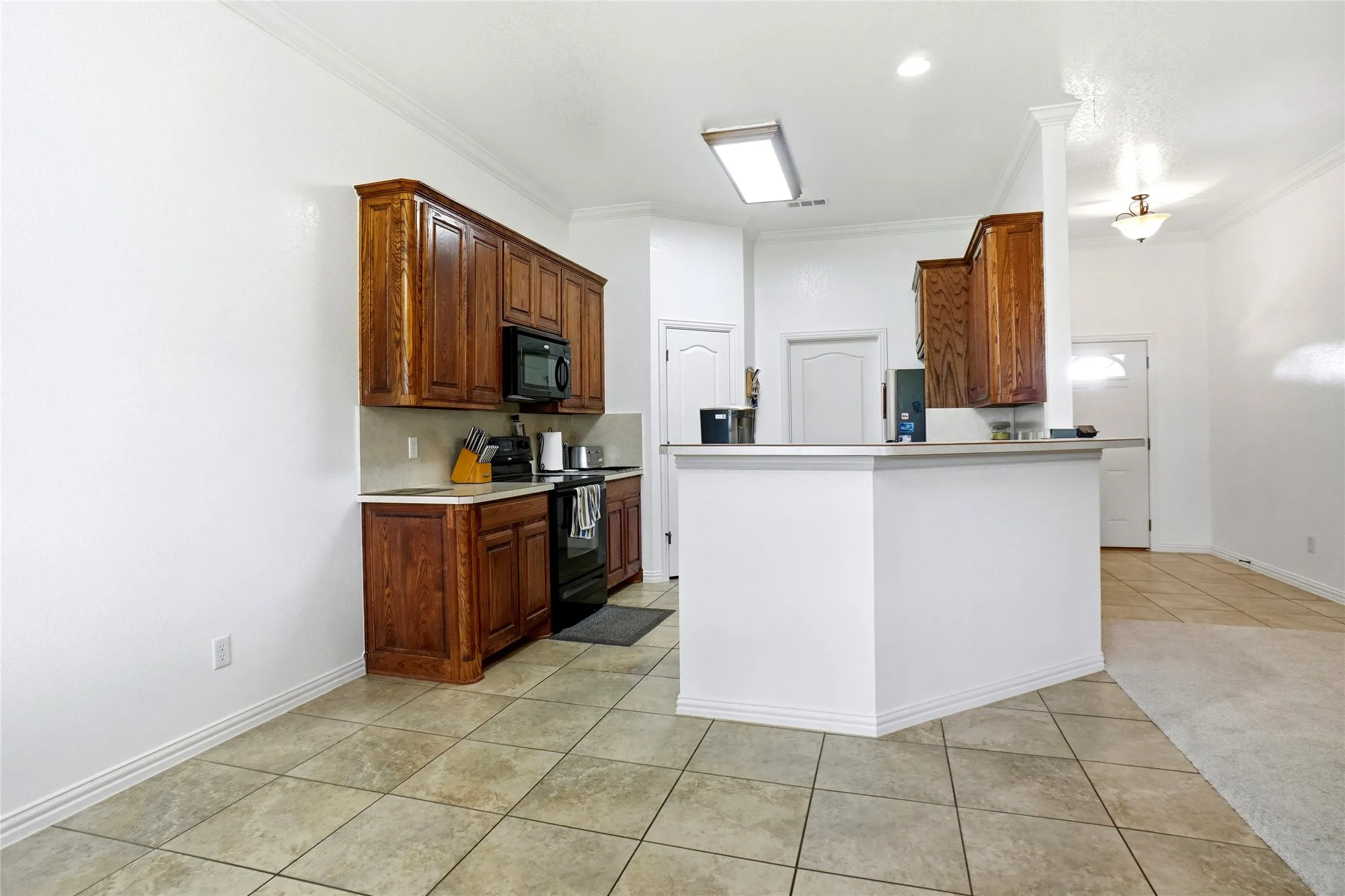 Kitchen featuring rich wood cabinetry, black appliances, light countertops, and a tiled floor