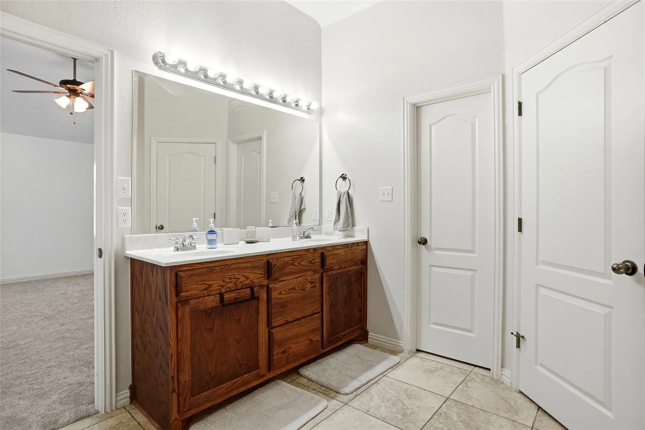 Dual vanity with wood-finish cabinetry, white countertop, and integrated sinks
