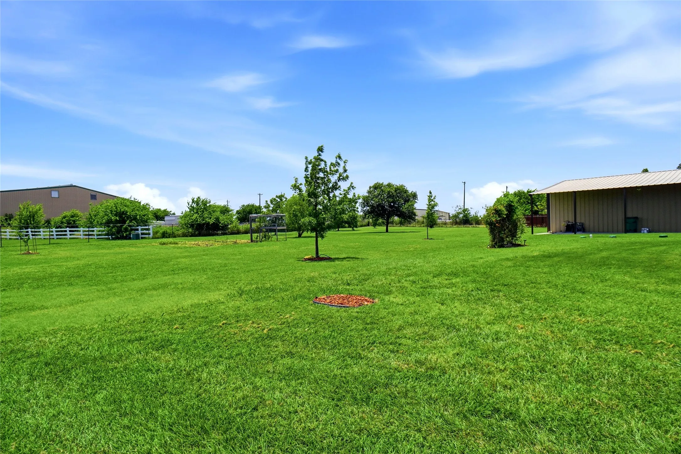 Expansive green lawn with mature trees and a white picket fence bordering the property