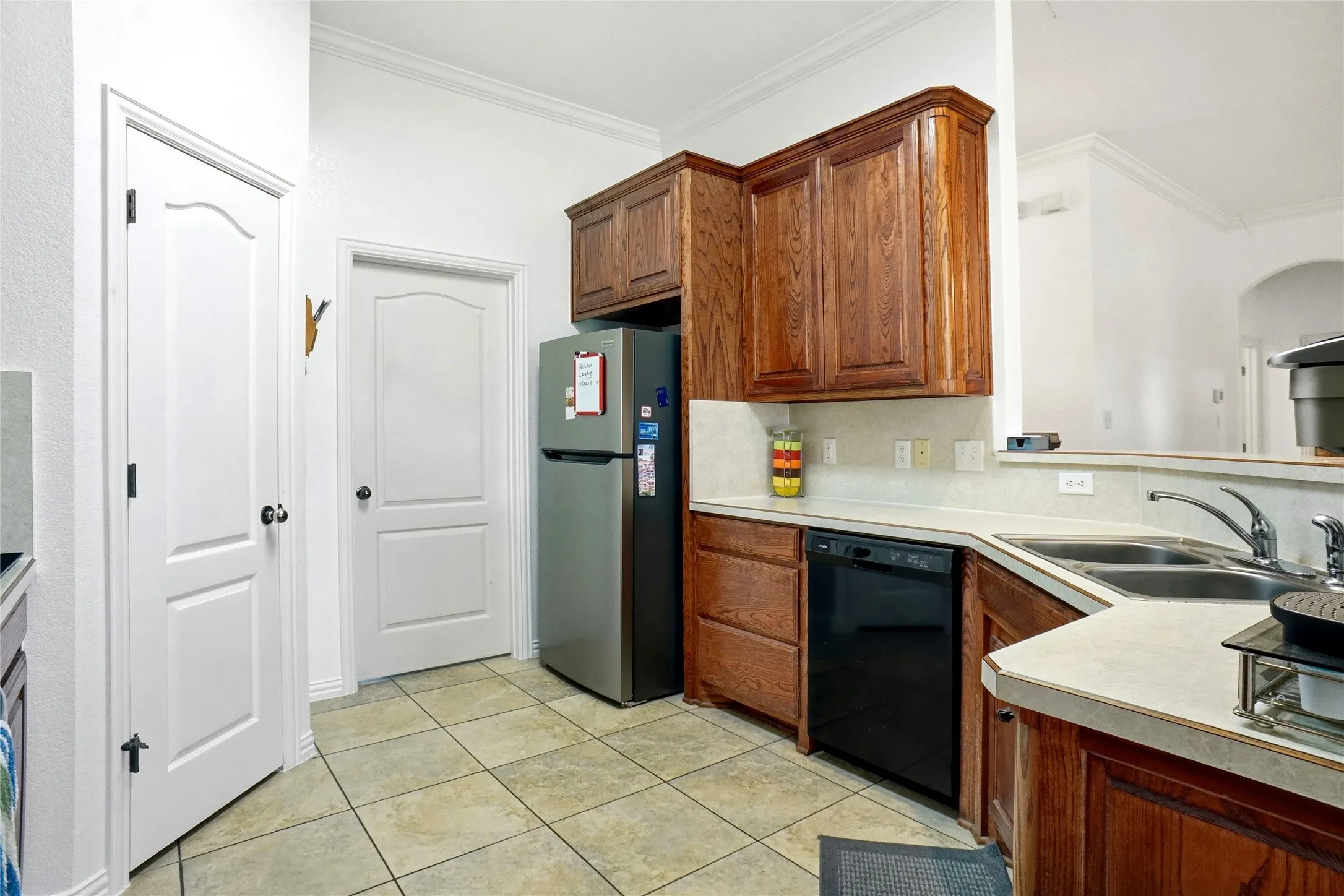 Kitchen featuring wood cabinetry, light-toned countertops, a double basin sink, and tile flooring