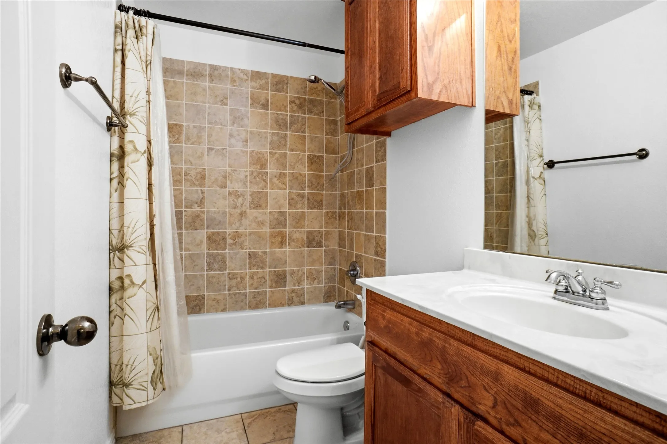 Bathroom featuring a bathtub with tile surround, wood-finish vanity, integrated sink with chrome faucet, and tile flooring