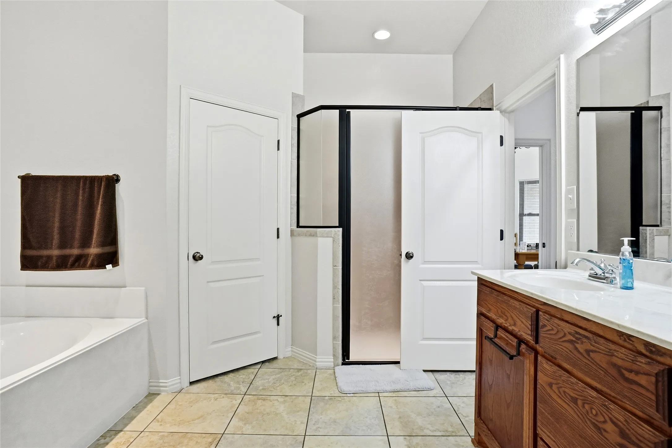 Bathroom featuring a corner soaking tub, a separate shower with a frosted glass enclosure, a single vanity with a wood-finish cabinet, and tile flooring