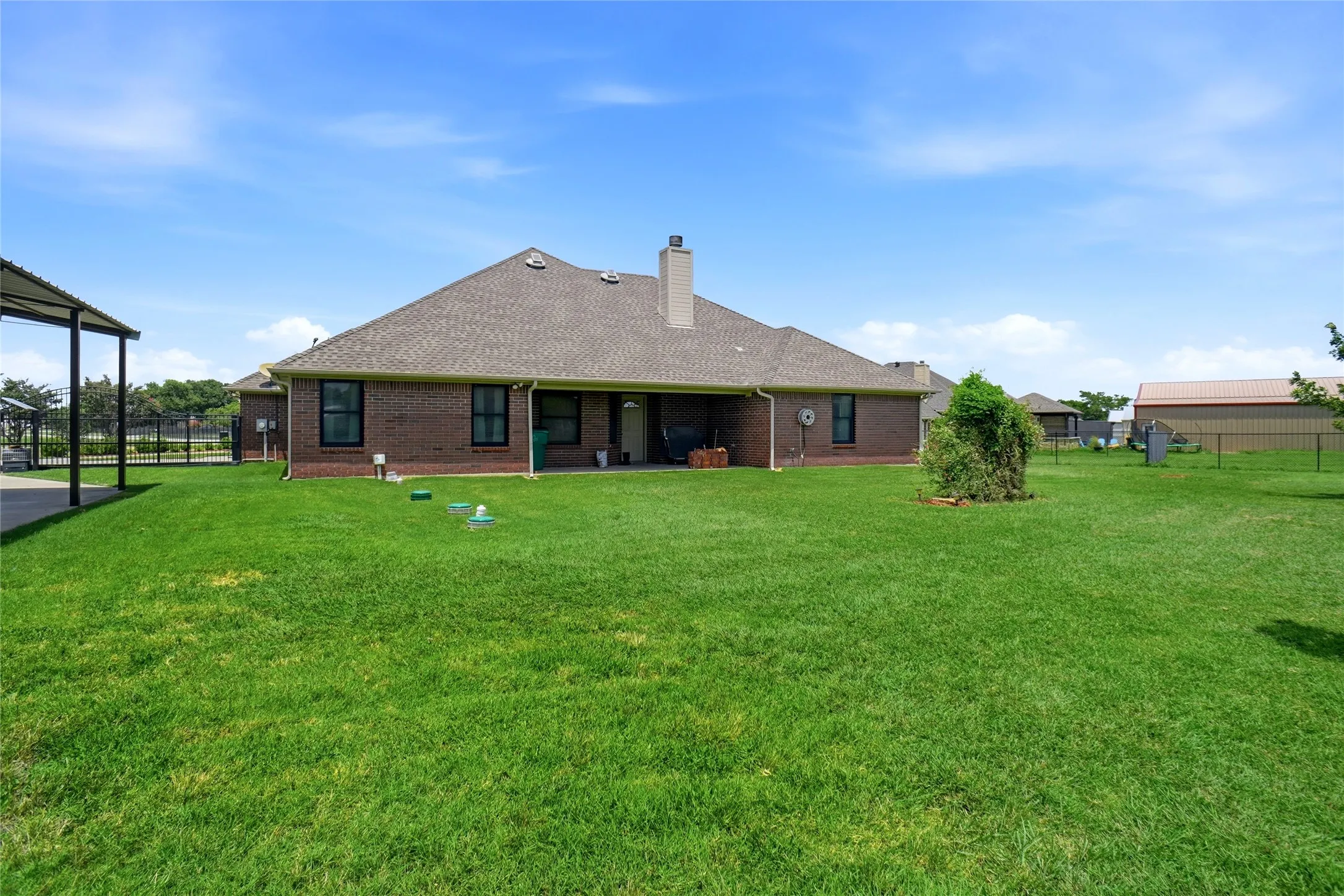 Extensive green lawn surrounding a brick exterior home with a covered patio