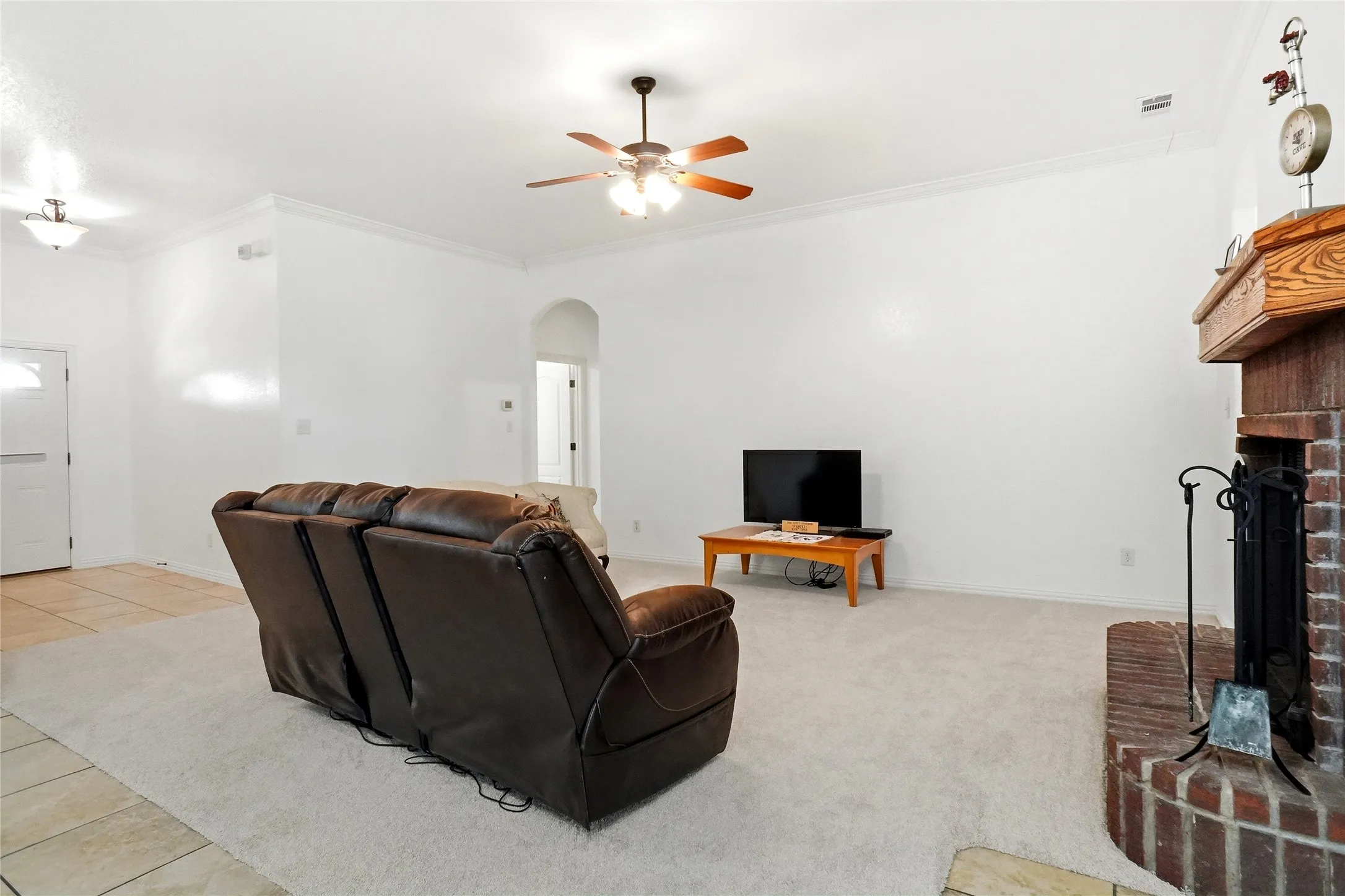 Spacious living area featuring a brick fireplace with a wood mantel, crown molding, and a ceiling fan with integrated lighting