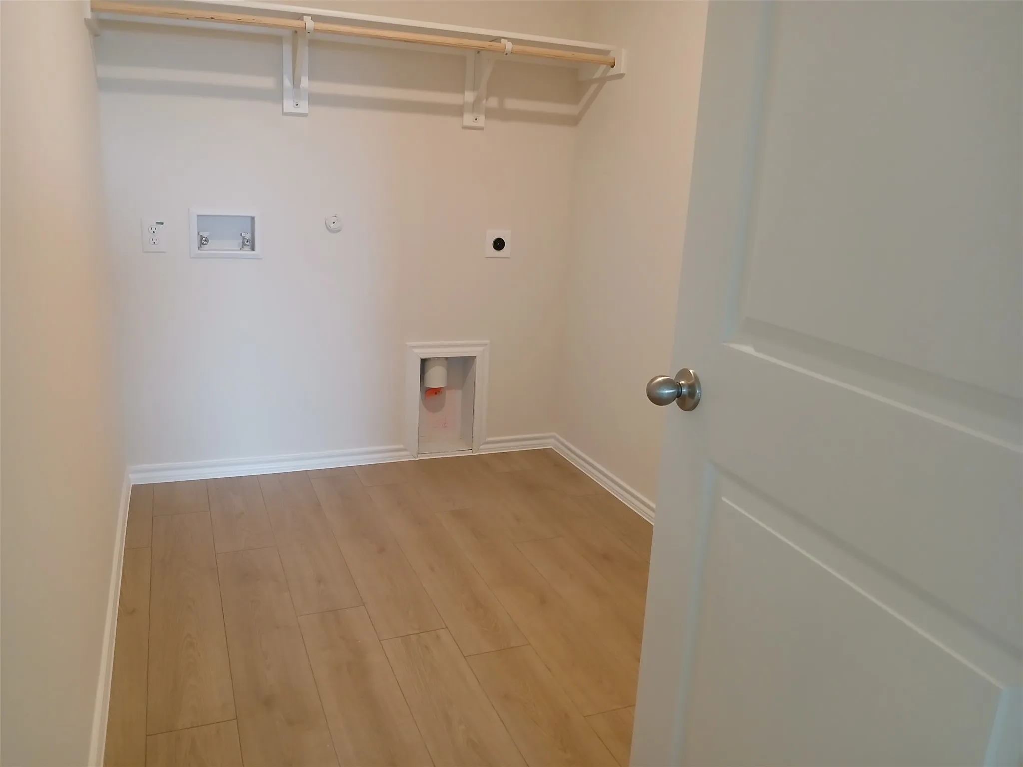 Dedicated utility space featuring light wood-finish flooring, white walls, and a built-in hanging rod