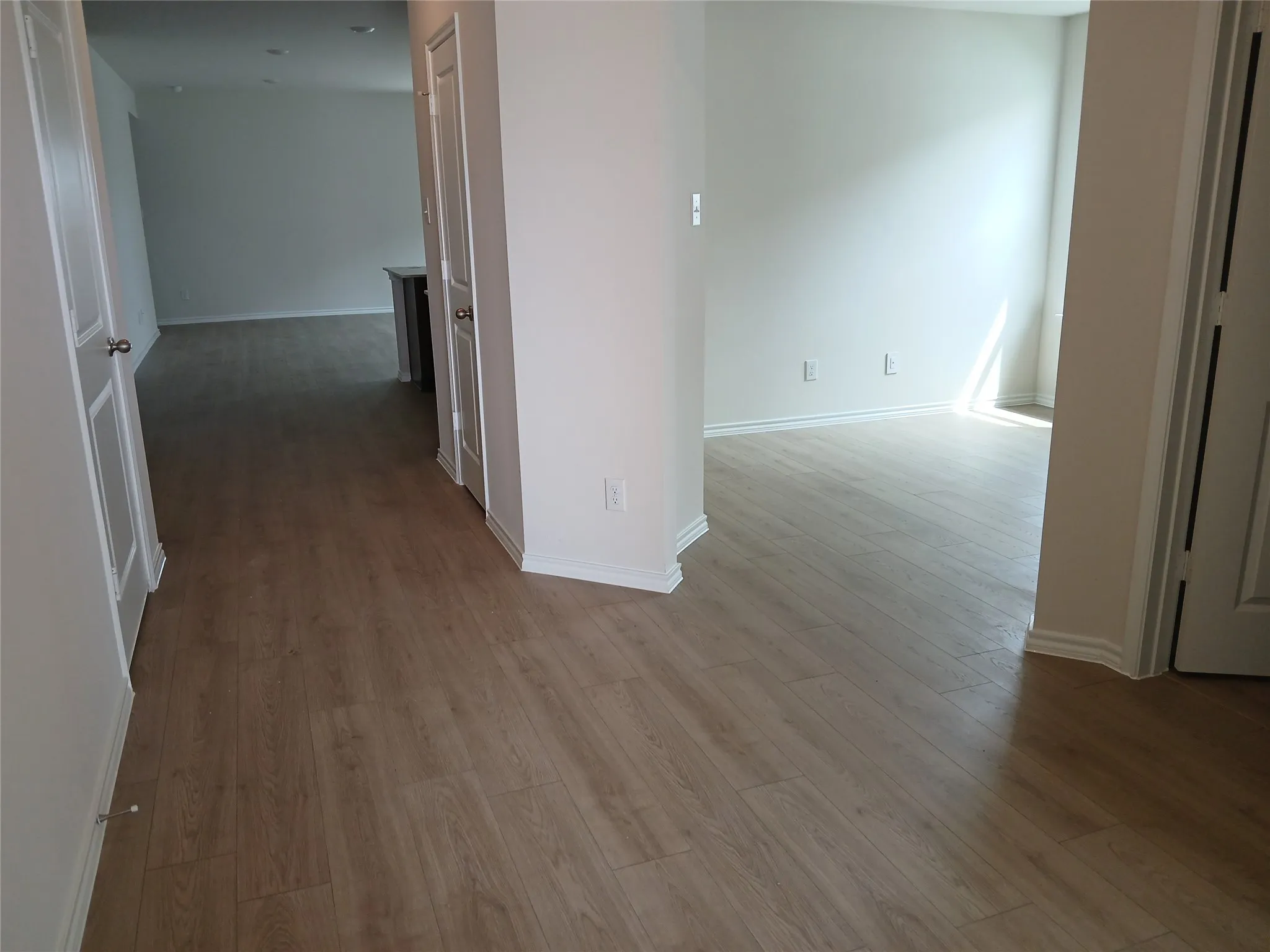 Light wood-finish flooring extends through multiple rooms, complemented by white walls and trim