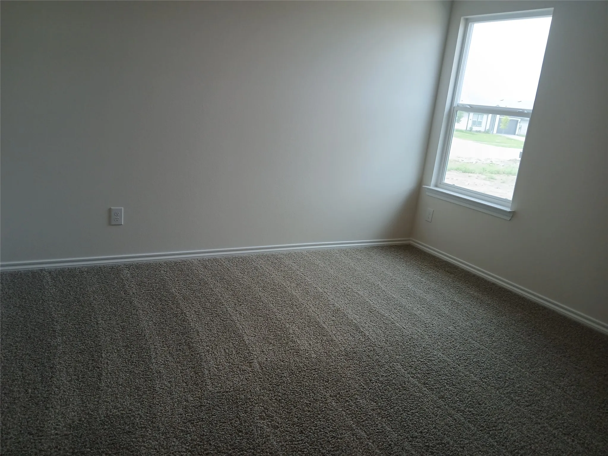 Neutral tone wall paint, textured carpeting, white baseboards, and a double-hung window with white trim