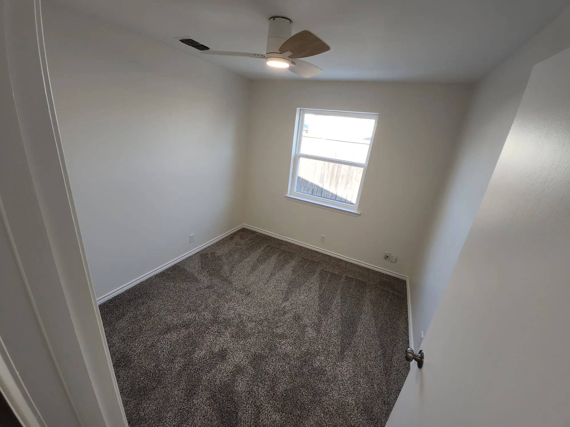 Neutral tone wall paint with white trim, a single window, and a ceiling fan with integrated lighting