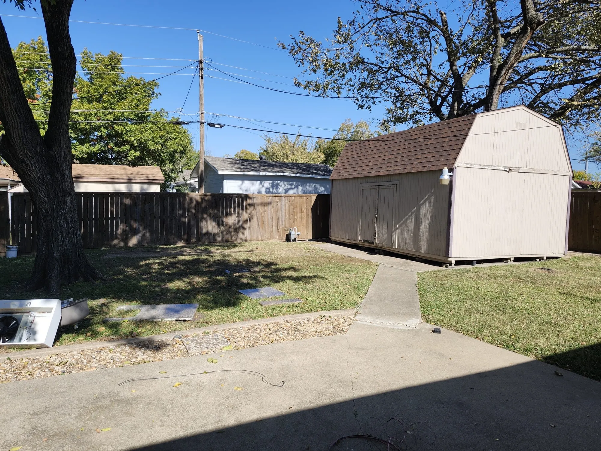 Backyard featuring a gabled shed with shingled roof, a paved patio, and a concrete pathway