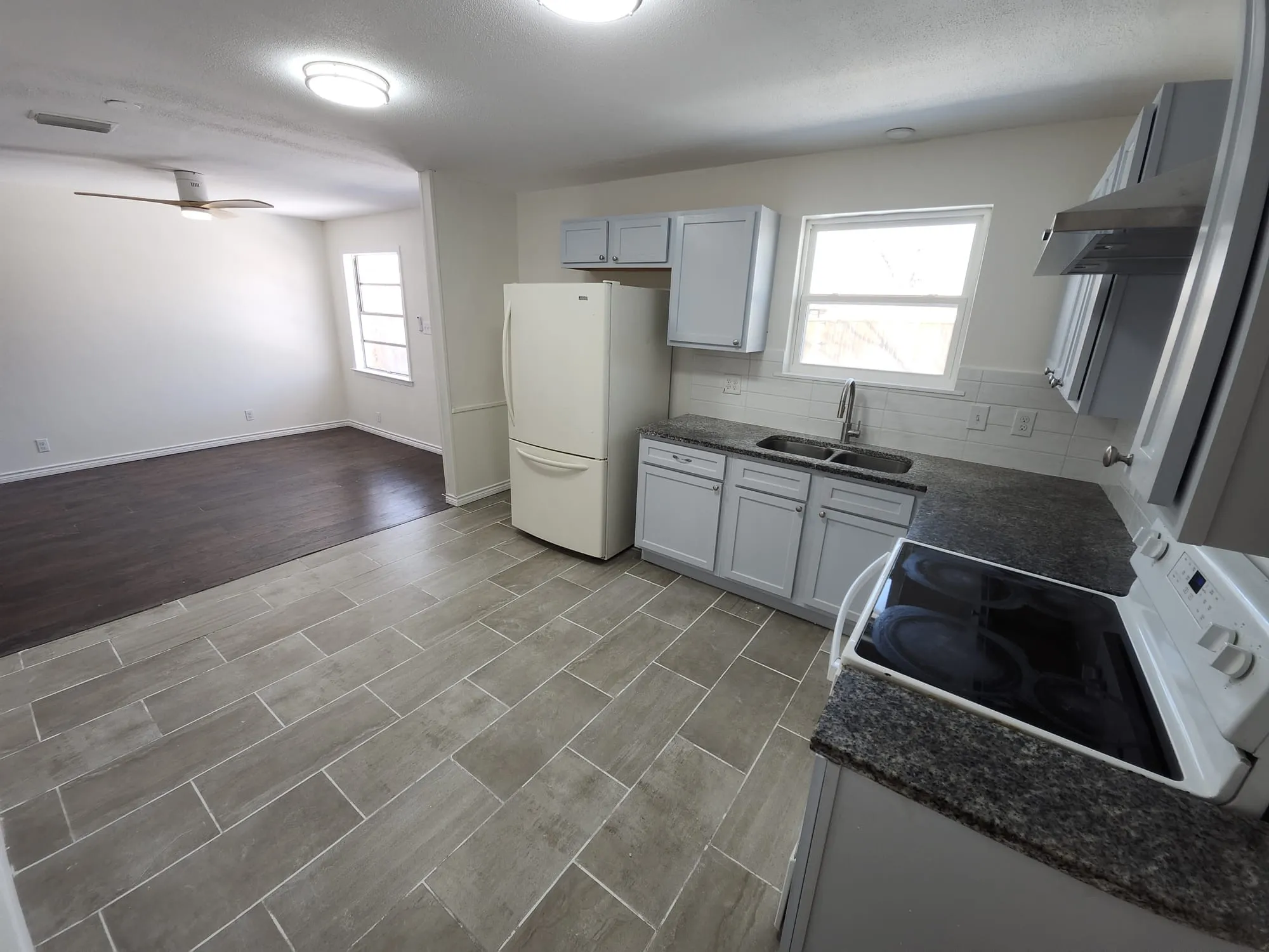 Kitchen featuring light gray cabinetry, dark speckled countertops, a double basin sink with a chrome faucet, a white subway tile backsplash, and a stainless steel range hood