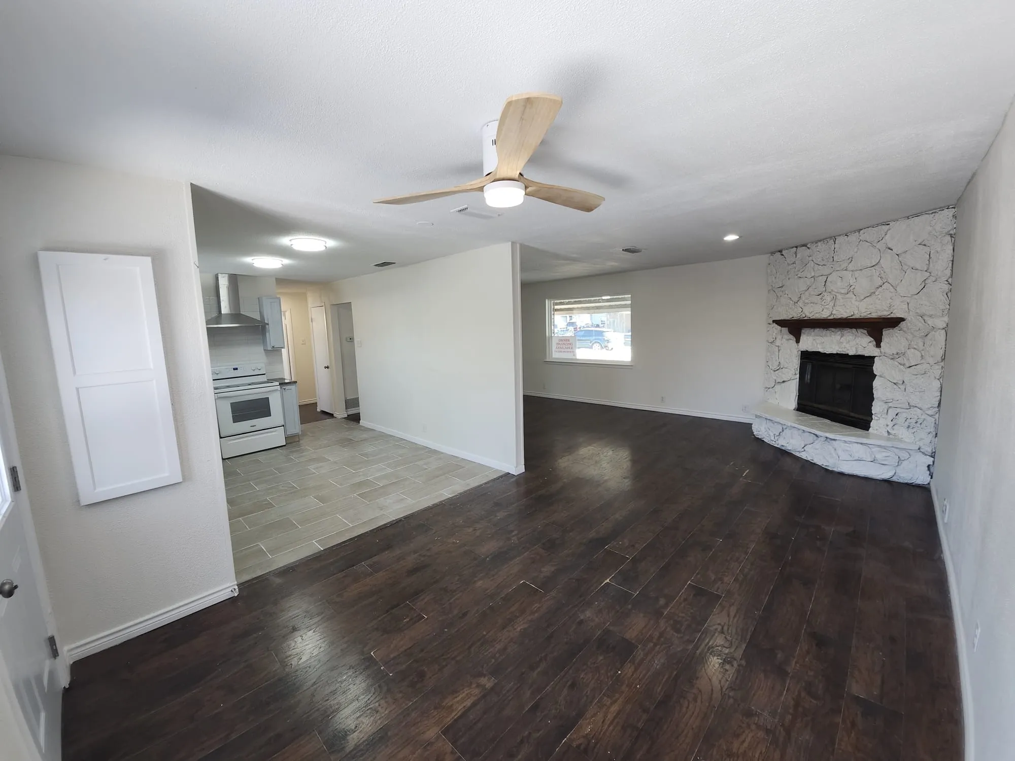 Spacious open-concept interior featuring dark wood-finish flooring, a white stone fireplace with a wood mantle, and a contemporary ceiling fan