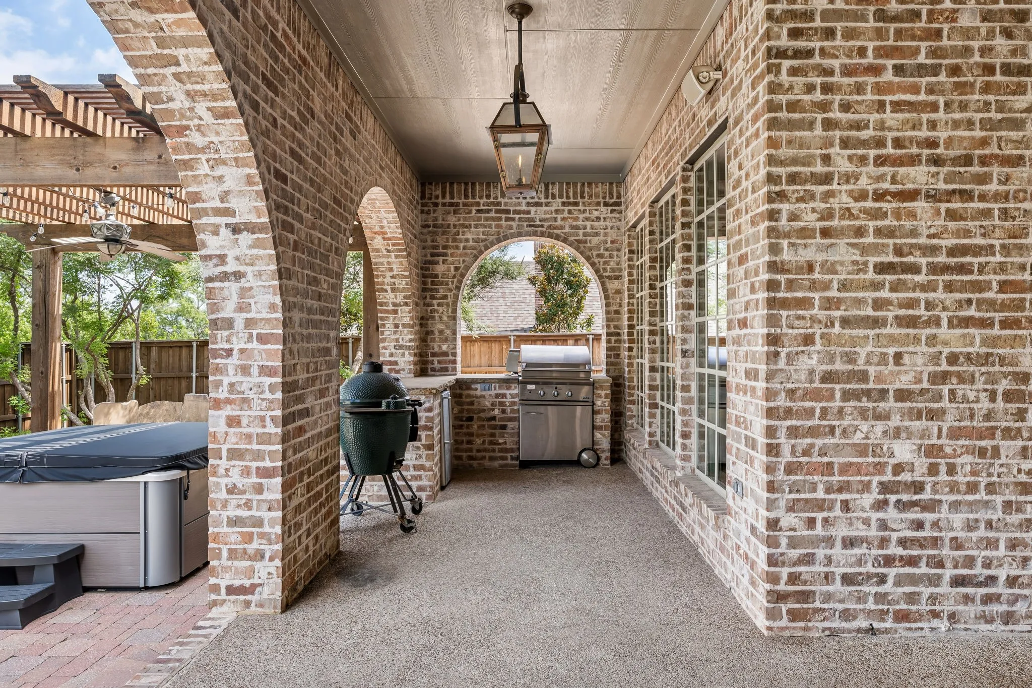 The covered patio features brick archways and a built-in outdoor kitchen with a grill.