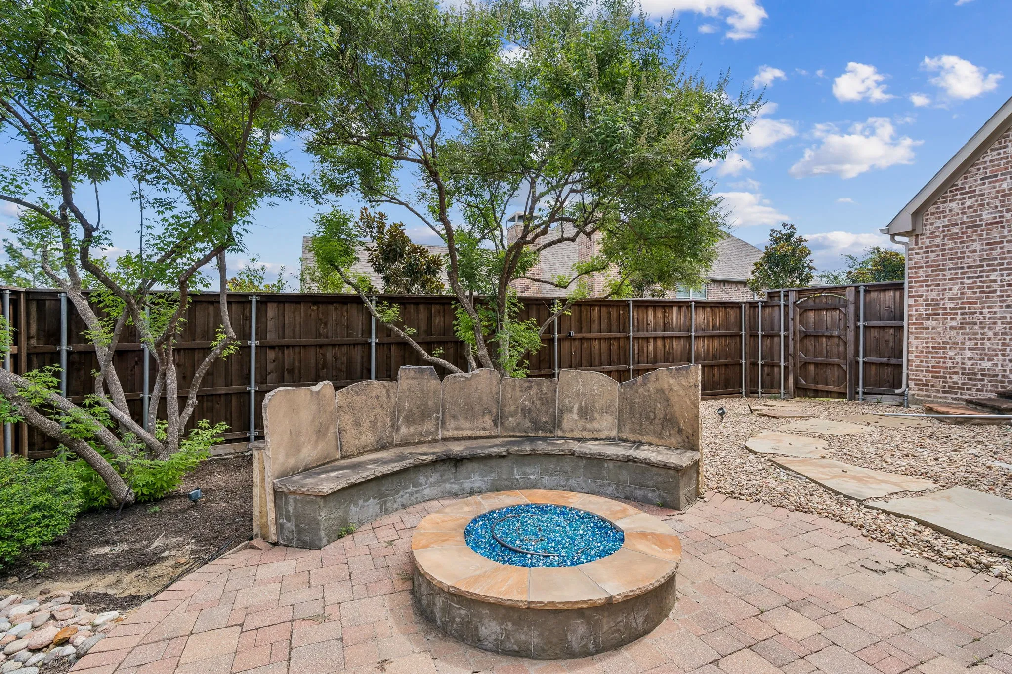 The outdoor living area features a built-in fire pit with blue glass media, a curved stone bench, and paver patio.