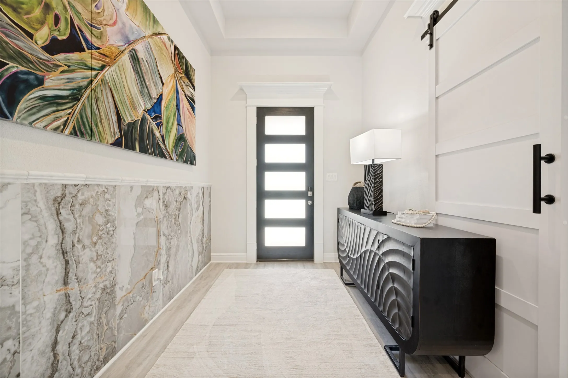 A dramatic foyer welcomes you with custom marble-inspired wall treatments, elevated architectural details, and a contemporary glass-panel front door. This thoughtfully curated space blends modern elegance with timeless design, creating a warm and sophisticated introduction to the home.