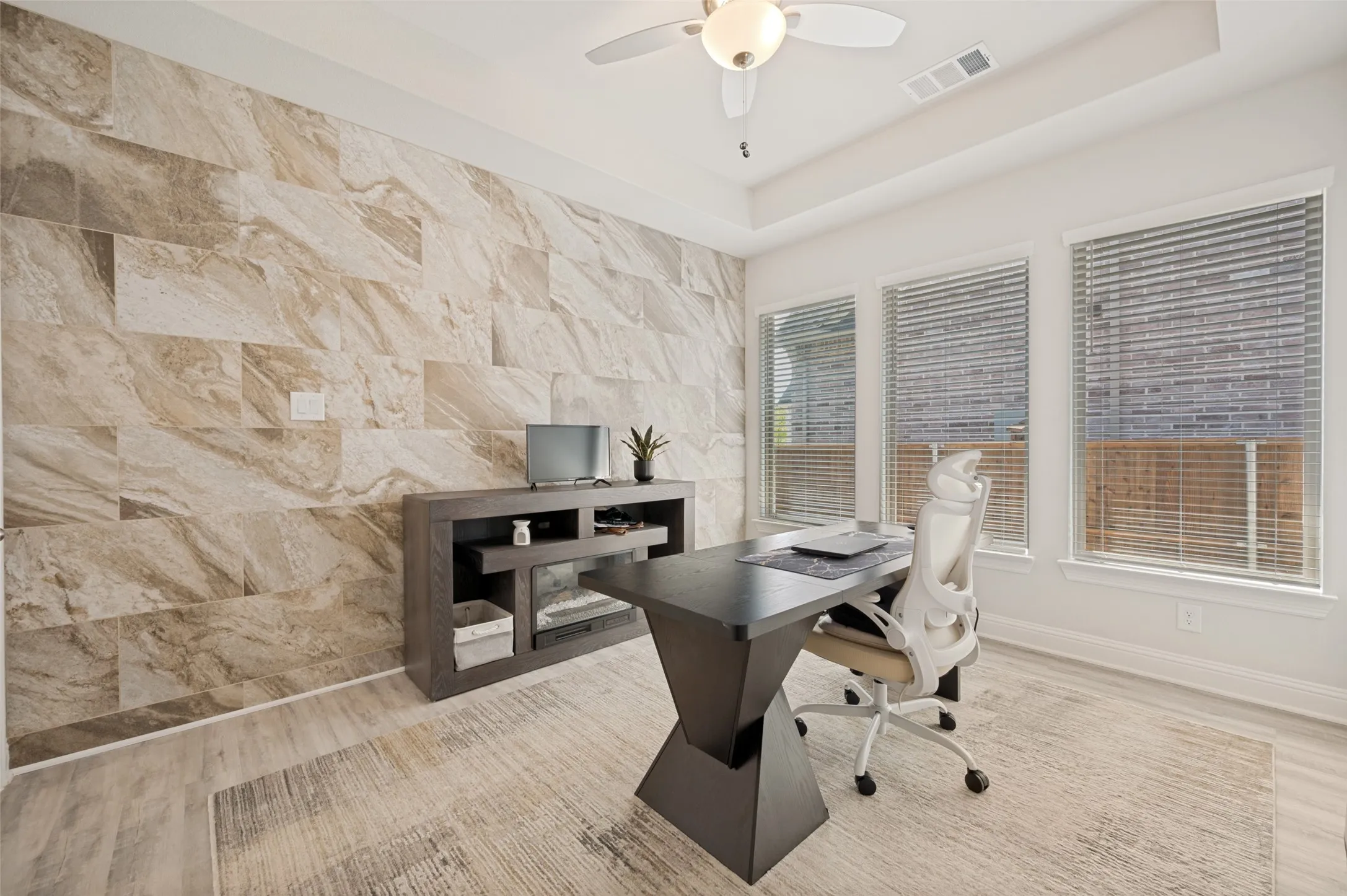 Beautiful home office featuring a dramatic custom stone accent wall, abundant natural light, and a sophisticated workspace perfect for working from home. The designer finishes create a productive and inspiring environment while adding a unique architectural focal point.