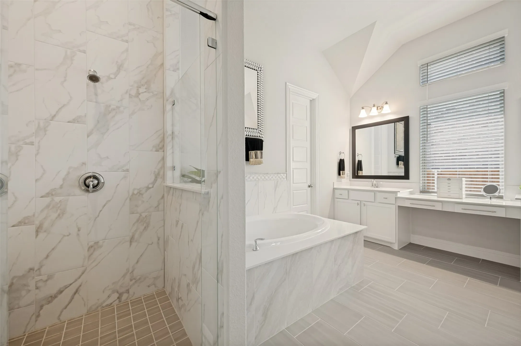 Experience luxury every day in this stunning primary bathroom featuring a frameless glass walk-in shower with floor-to-ceiling marble-look tile, a relaxing garden tub, and soaring ceilings that create a bright, open feel. The extended vanity offers abundant storage and a dedicated makeup area beneath oversized windows that fill the space with natural light. Thoughtfully designed with elegant finishes and a timeless color palette, this spa-like retreat provides the perfect place to begin and end your day.
