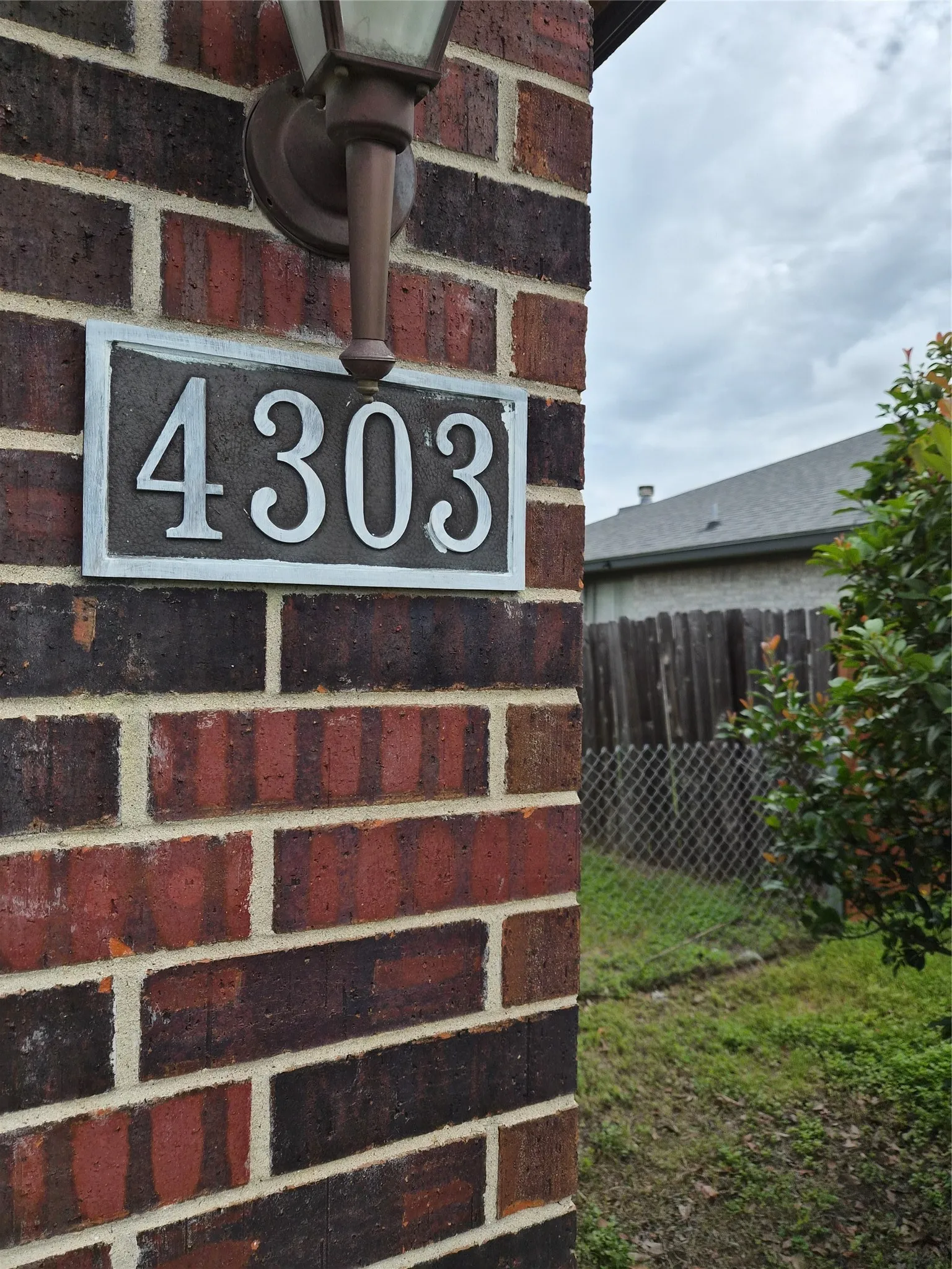 Brick exterior column featuring an attached wall lantern and prominent house number plaque
