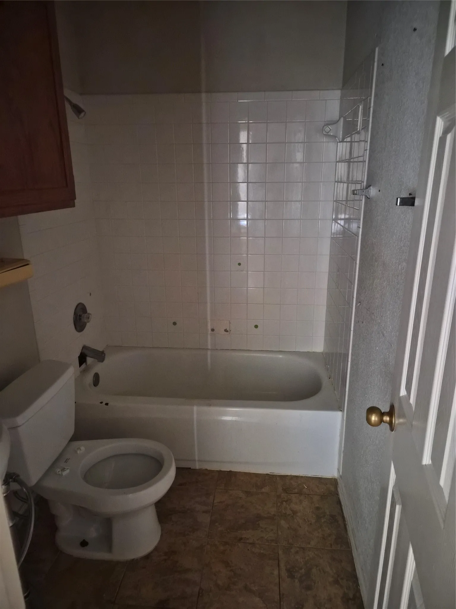 White tiled shower surround with a built-in tub, complemented by a white toilet and brown-toned floor tiles