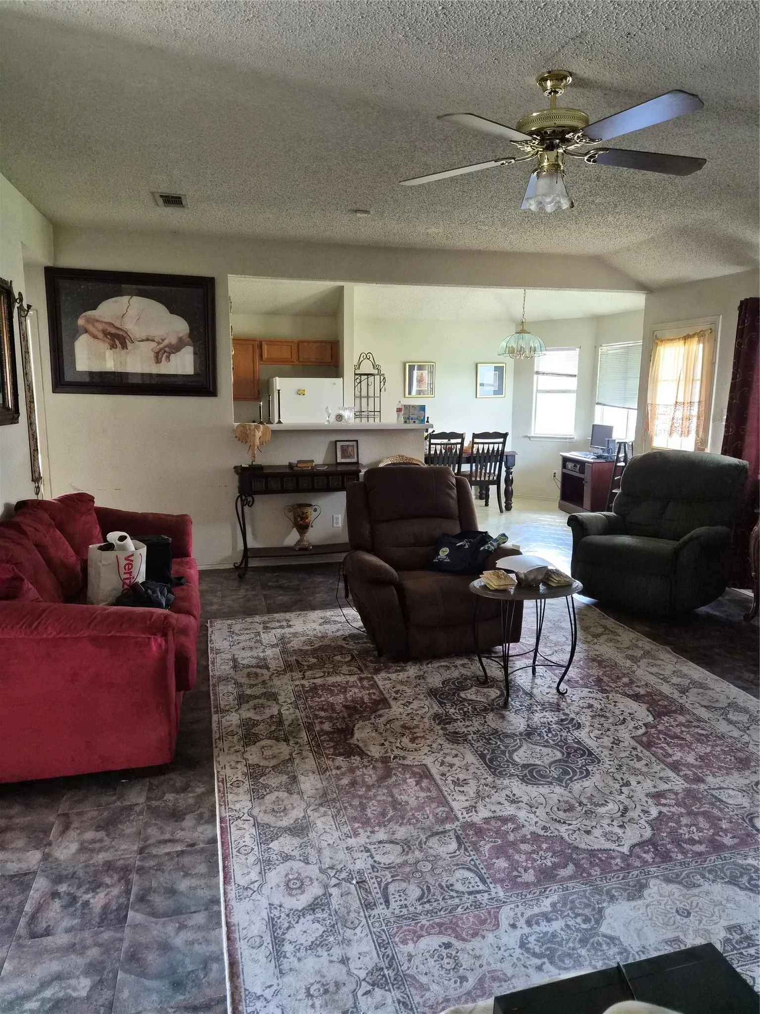 Open concept living area with tiled flooring, a ceiling fan, and a pass-through opening to the kitchen featuring wood-finish cabinetry
