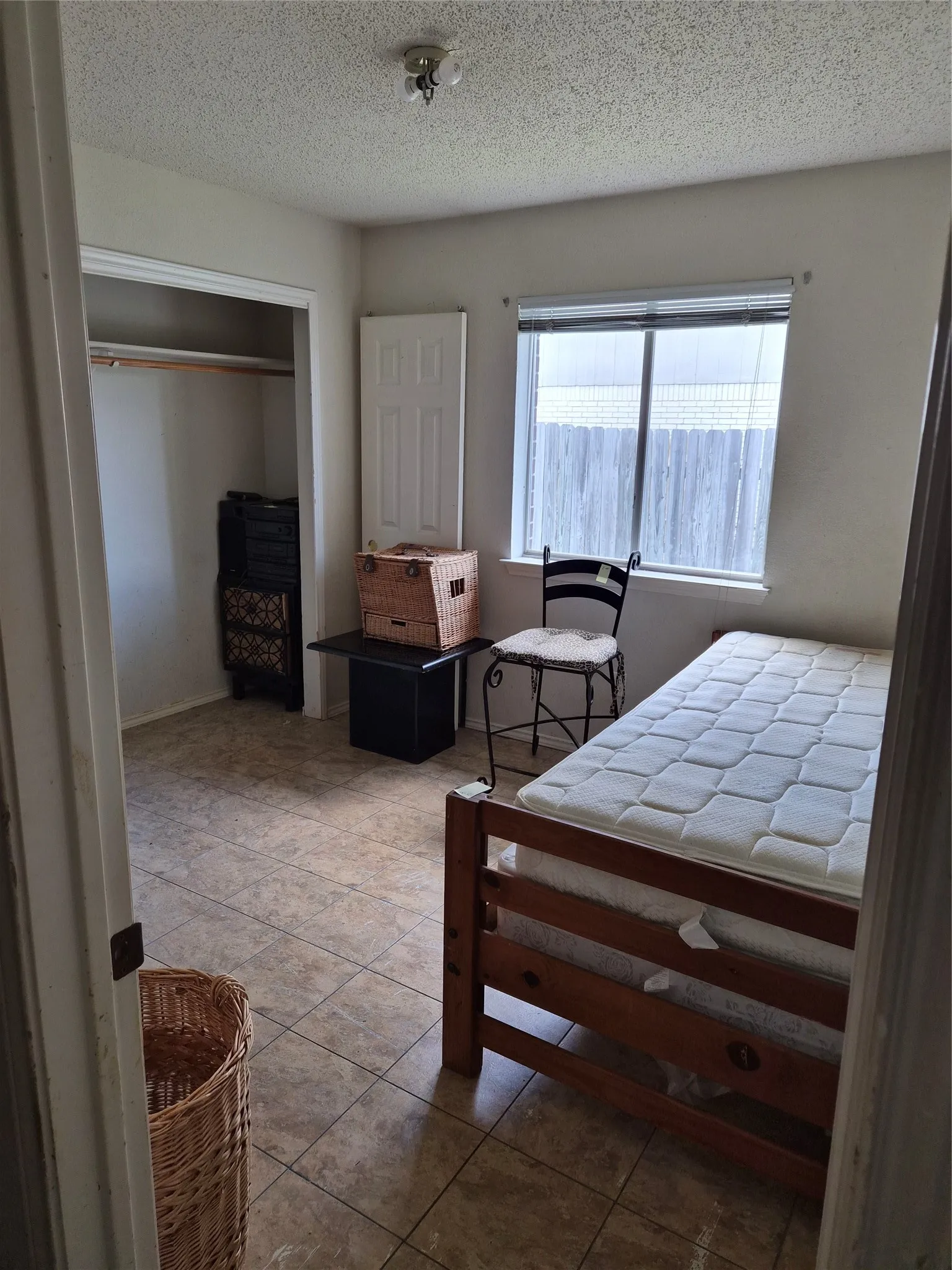 Room featuring tiled flooring, a window with horizontal blinds, and a built-in closet with a hanging rod