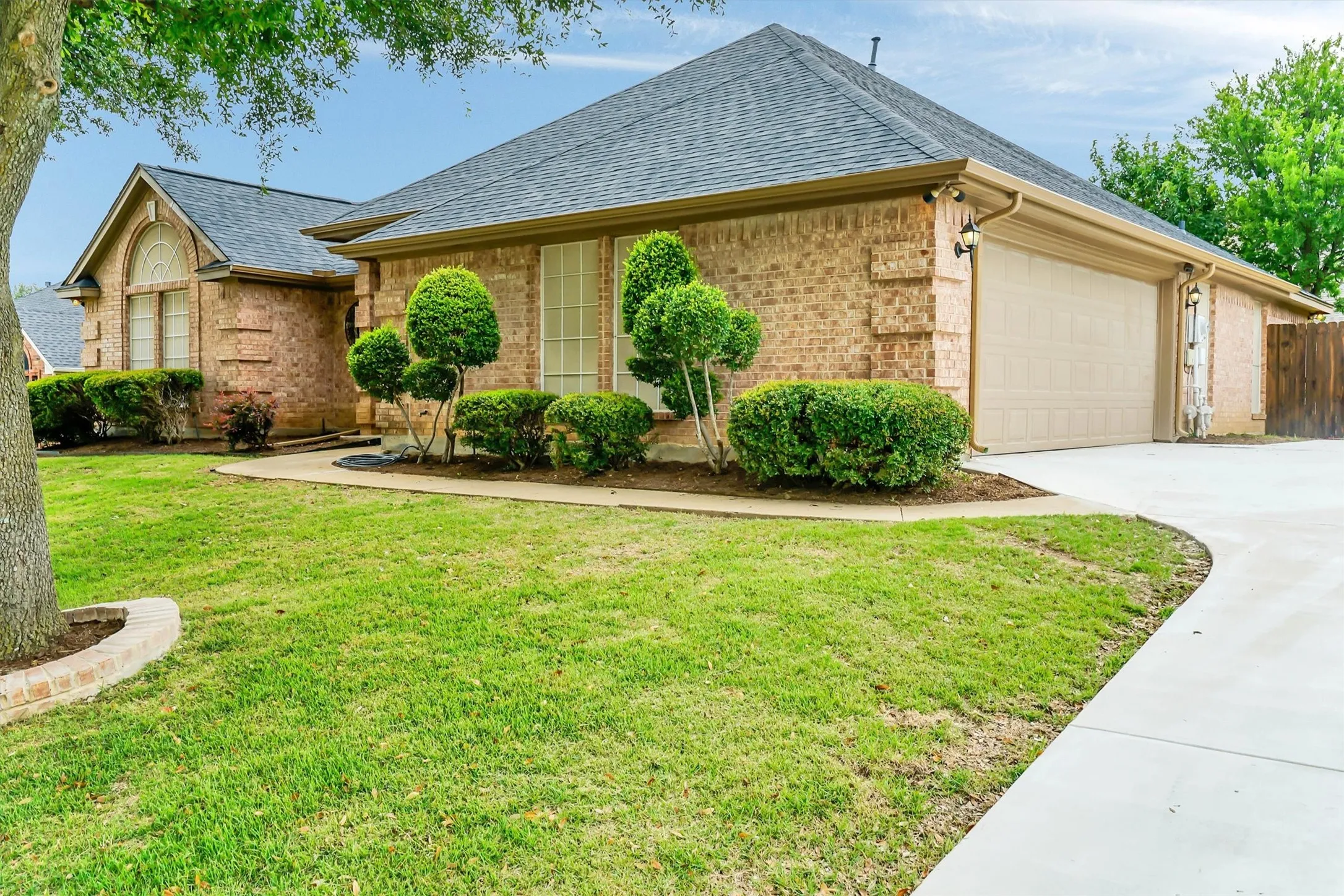 Traditional brick exterior featuring a multi-gabled roofline, an attached two-car garage, and a curved concrete driveway