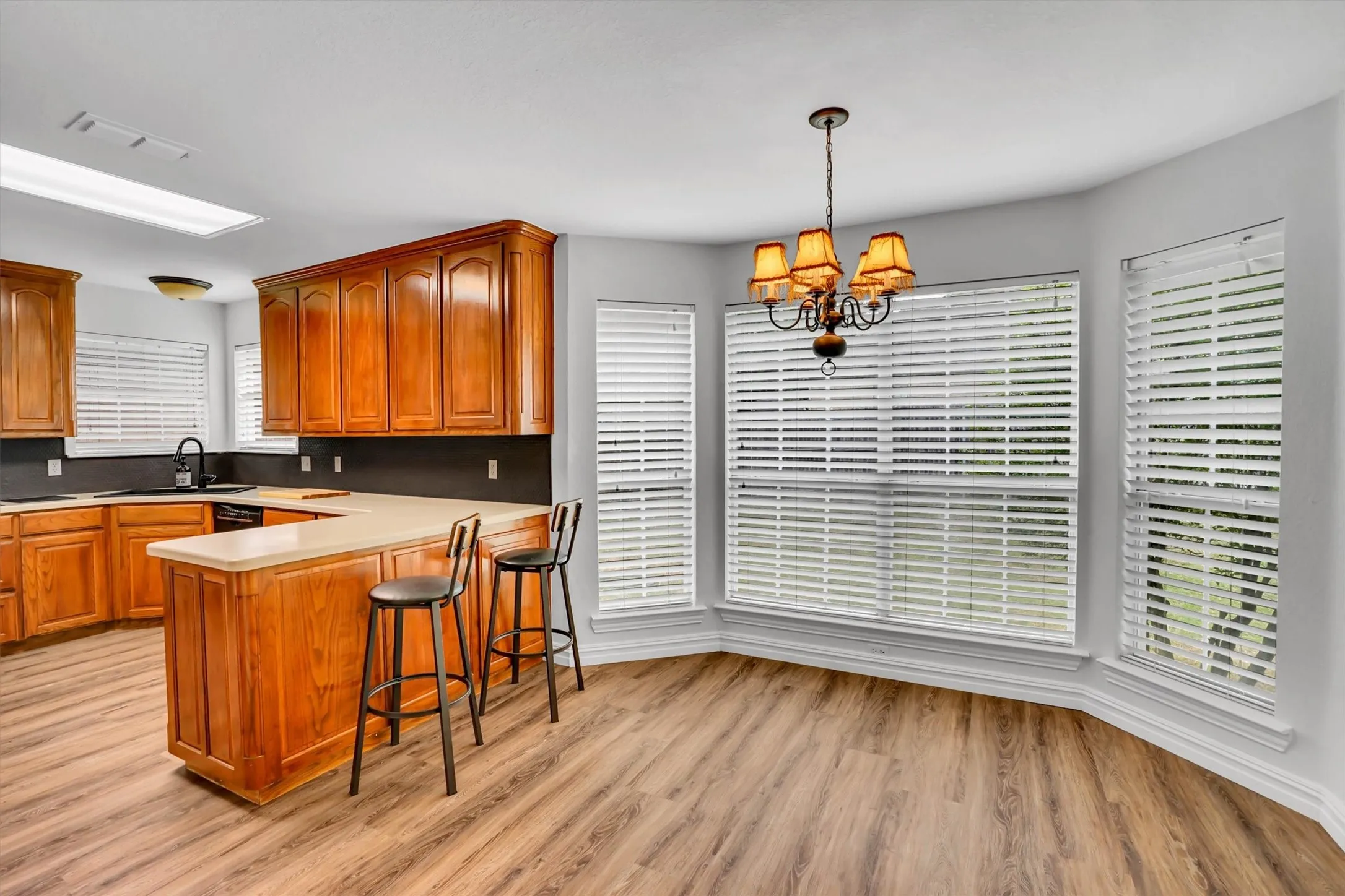 Kitchen featuring wood-finish flooring, light-toned countertops, dark backsplash, and rich wood cabinetry