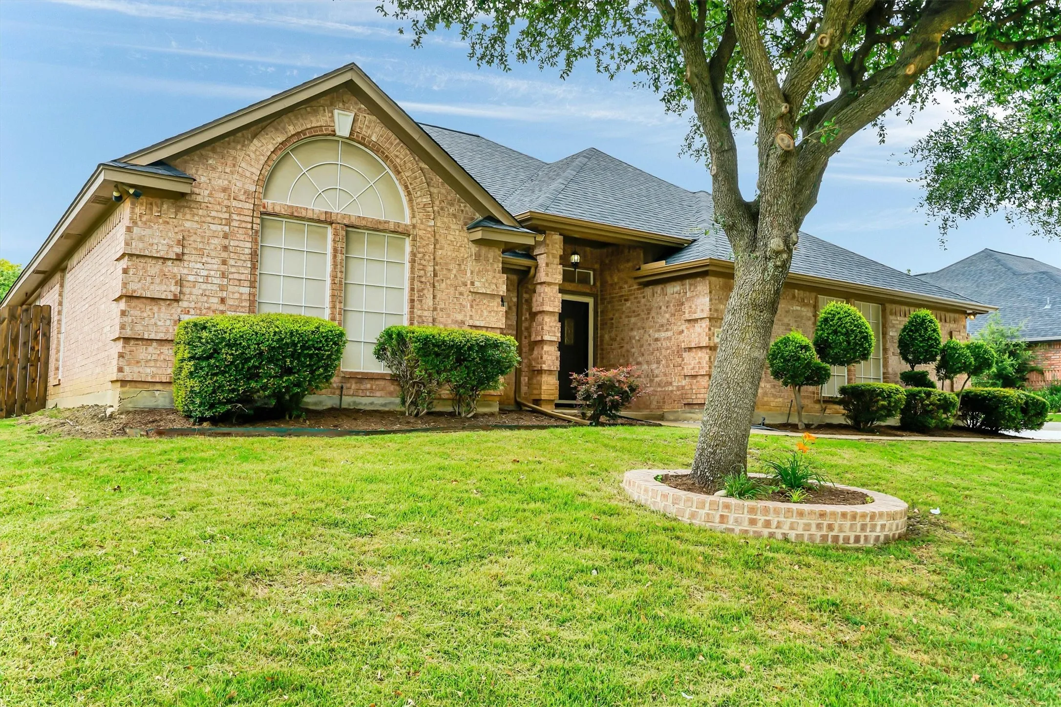 Traditional brick exterior with an arched transom window, a dark-toned entry door, a low-pitched roofline, and established front landscaping
