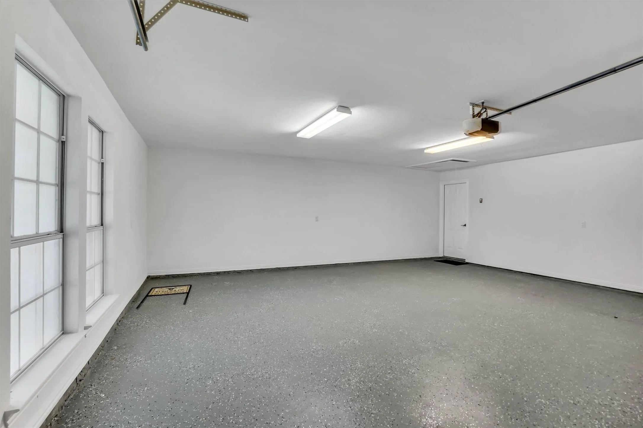 Spacious garage featuring a durable speckled epoxy floor, white painted walls, and ample natural light from two multi-pane windows