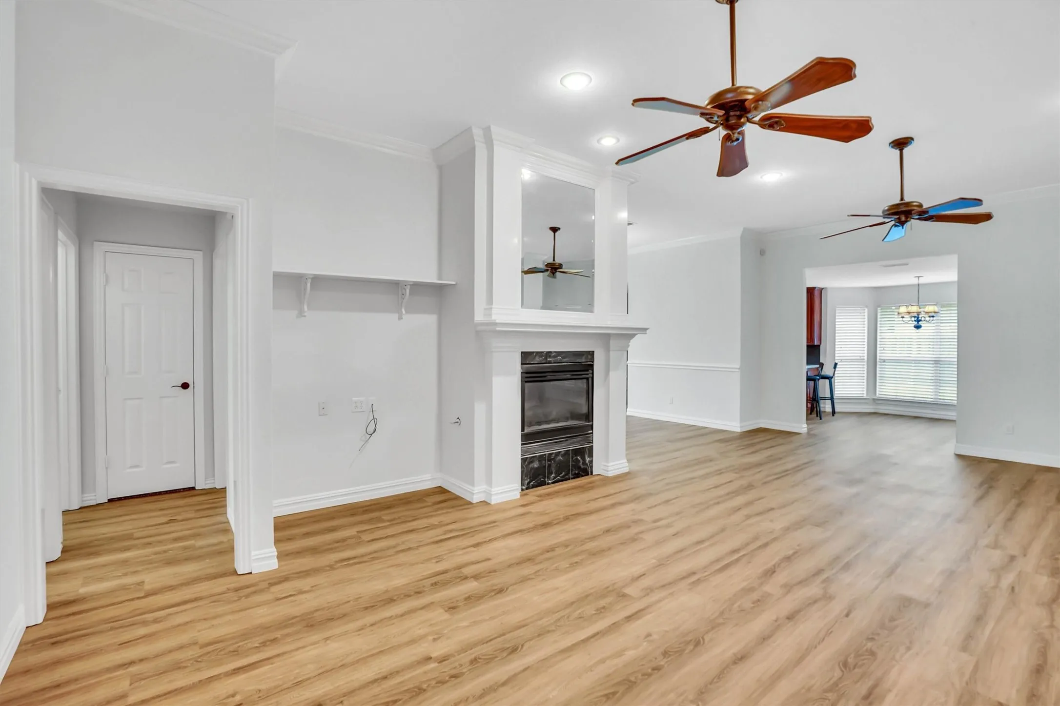 Spacious living area featuring light wood-finish flooring, a central fireplace with a white mantel, and crown molding
